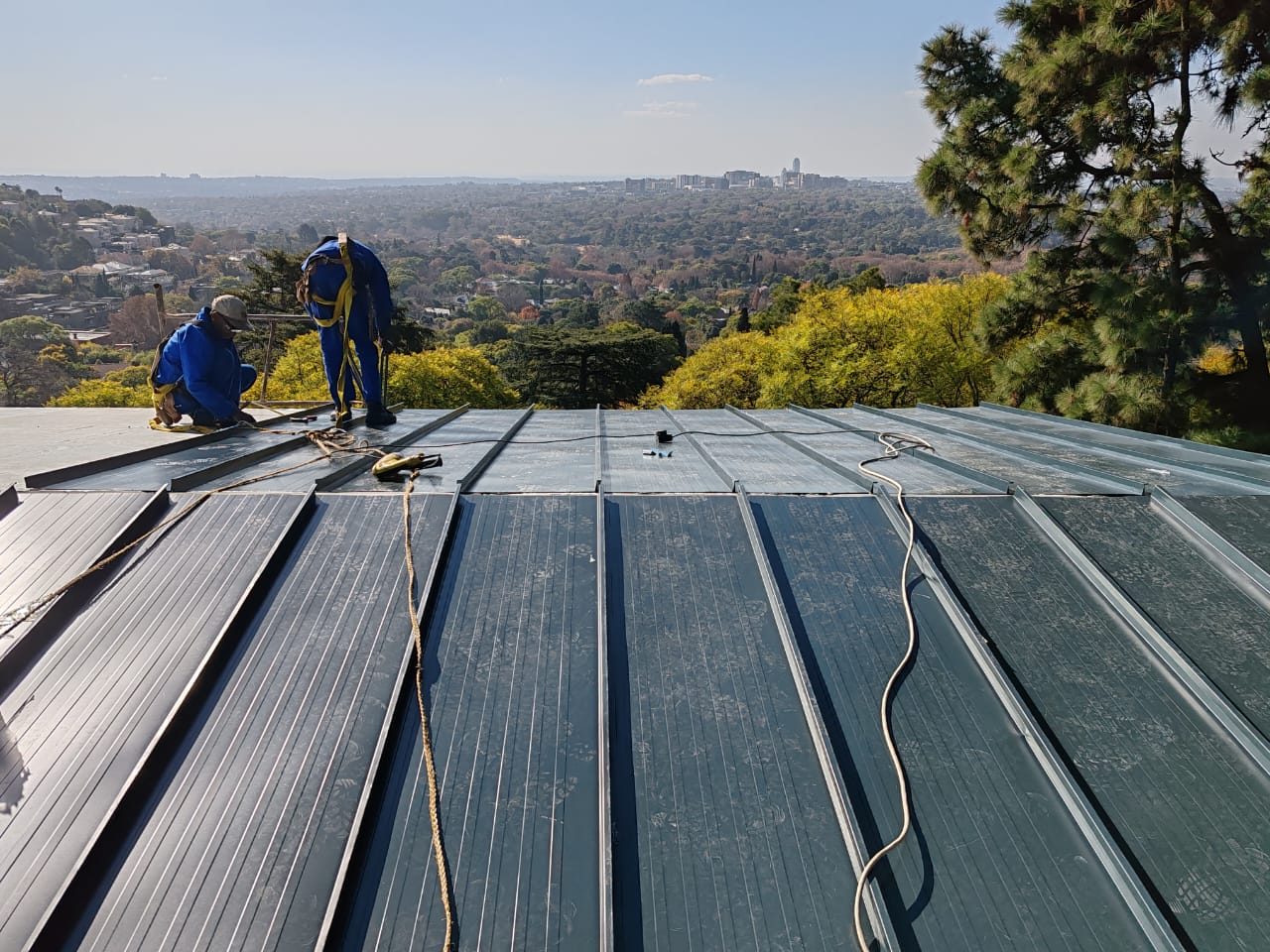 LiteSpan 990 Standing Seam being laid. The seams run up the slope with the holding clips concealed beneath them; there is not one fastener head in the field of the roof.
