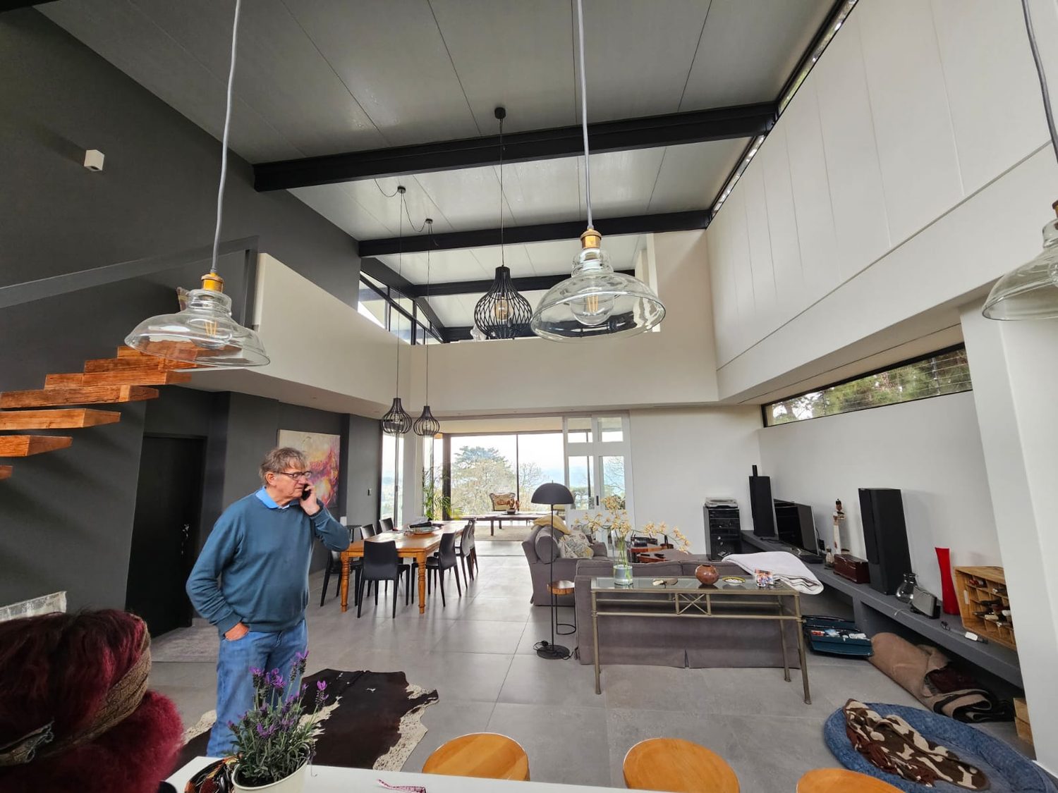 The same panel from inside. The finished ceiling of the double-volume living room is the underside of the roof — white factory skin, panel joints as the ceiling joints, steel beams below it. No ceiling board, no separate insulation layer.