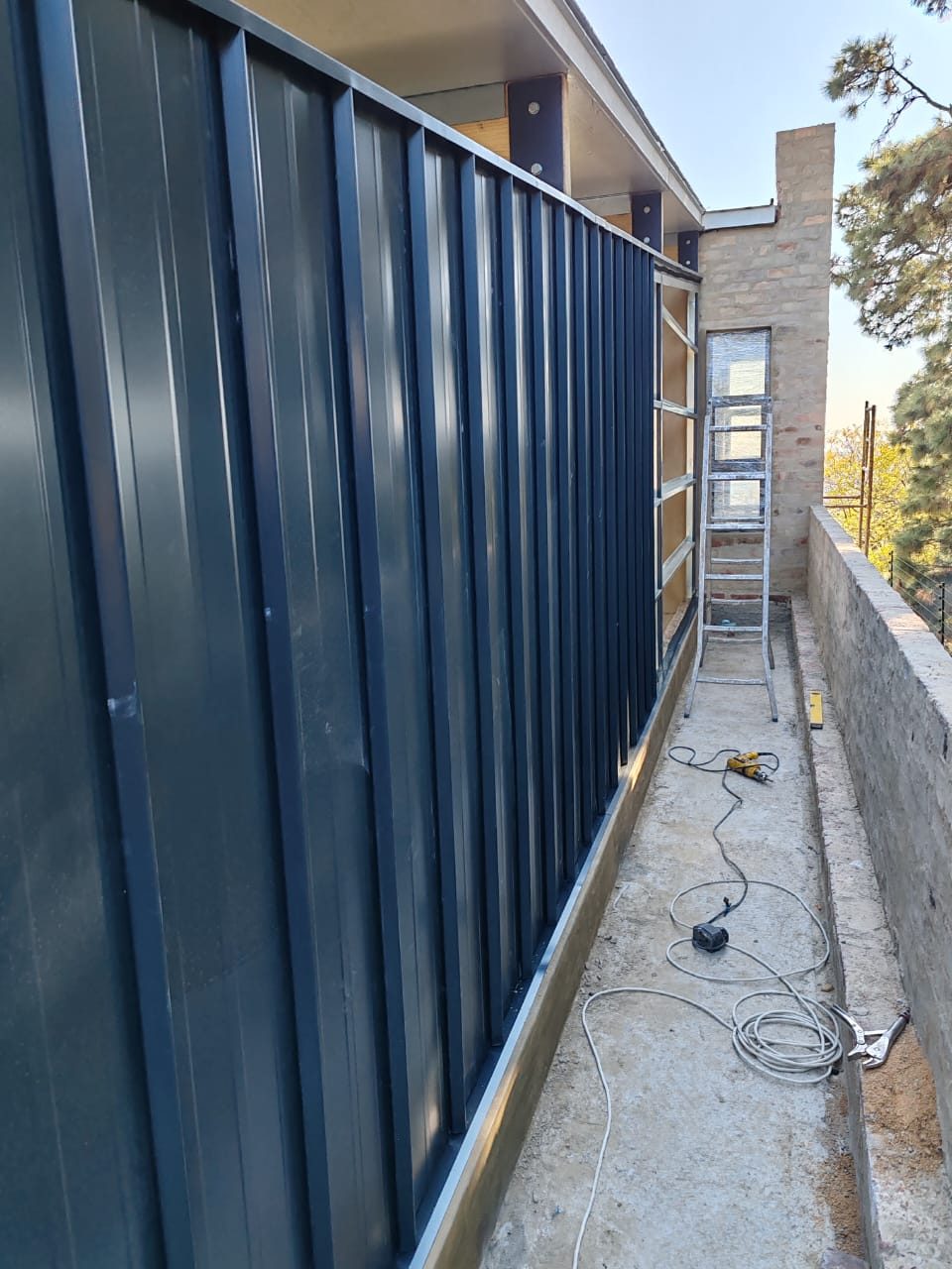 LiteClad ClipClad part-laid. Vertical profile, concealed wafer-screw fix — the completed run shows no fasteners on the face, while the unclad section still shows the rails it lands on.