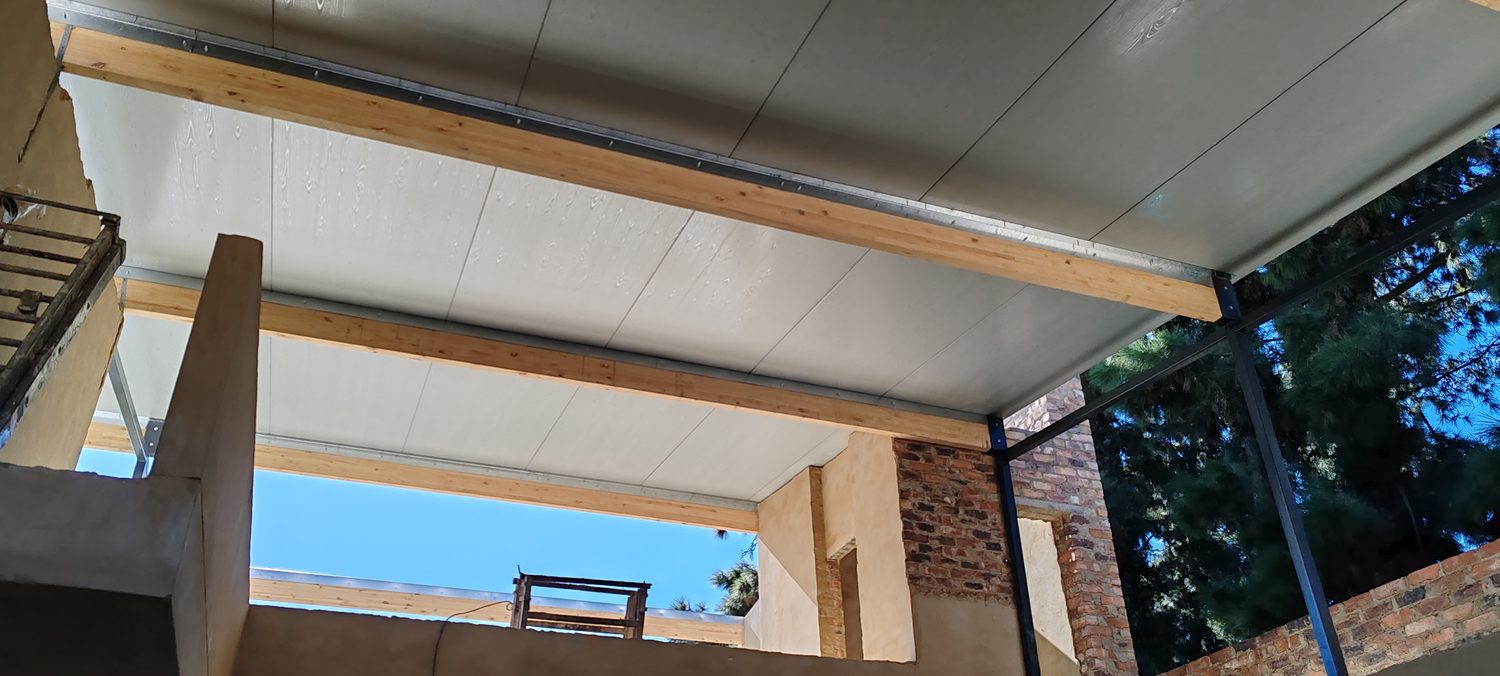 The soffit during construction, at the stage where a ceiling would normally start. The panels bear straight onto the timber, the white face is the finish, and the clerestory strip runs under the panel edge.