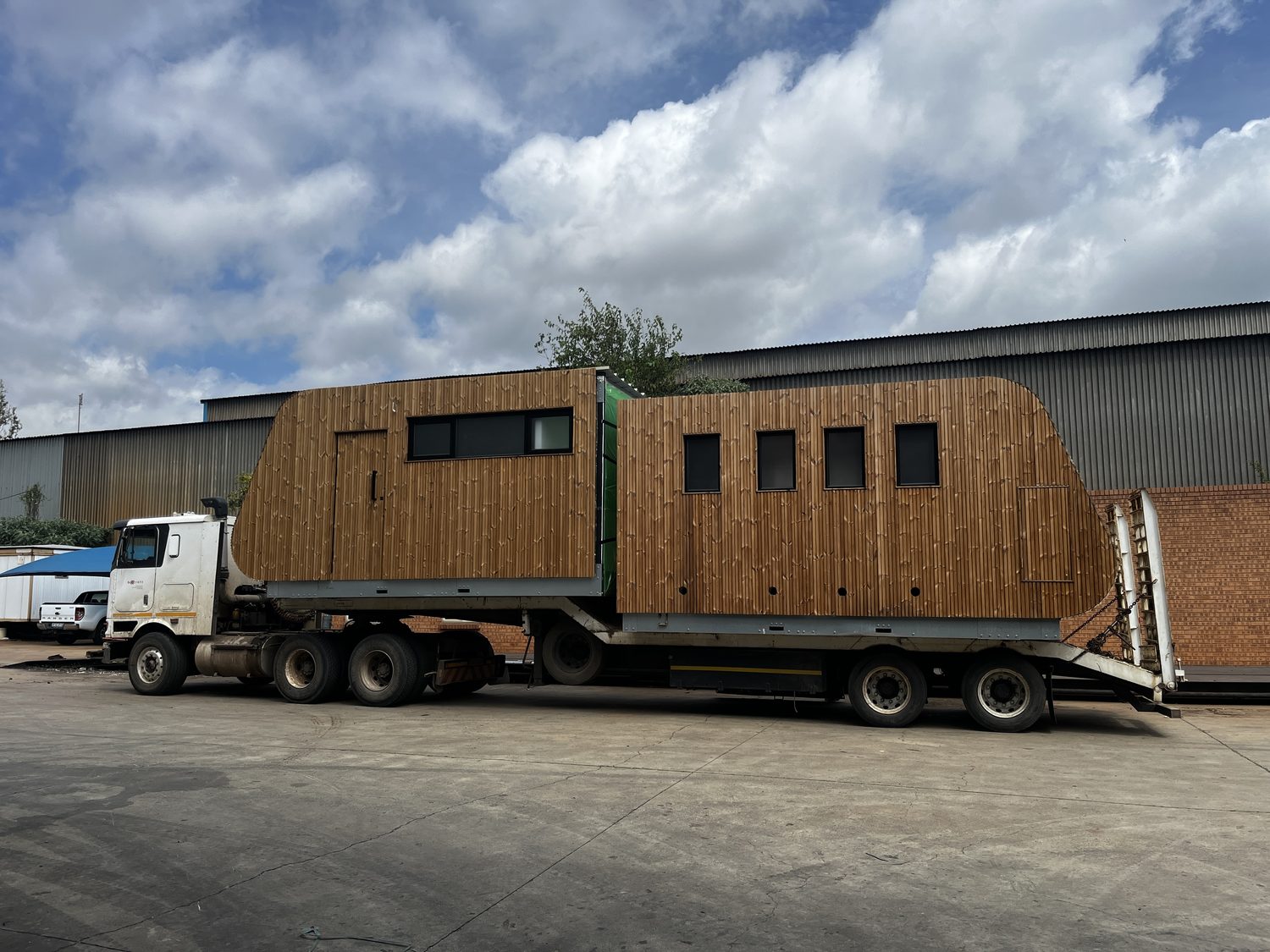 The finished unit on a lowbed — windows glazed, timber rainscreen on, doors hung. This is the load case that matters: the frame and the panel envelope have to take lifting and road transport without racking or opening a joint.