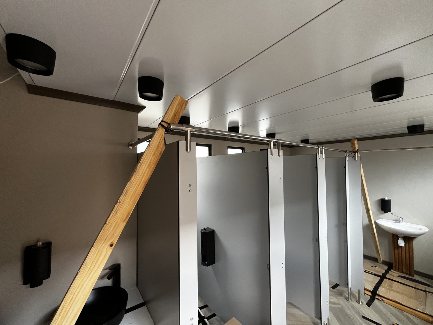 The ablution ceiling is the roof panel seen from below: flat white skin, joint lines visible. Note every light fitting is surface-mounted — recessed downlighters are not permitted in an EPS-core panel, and the detailing here respects that.