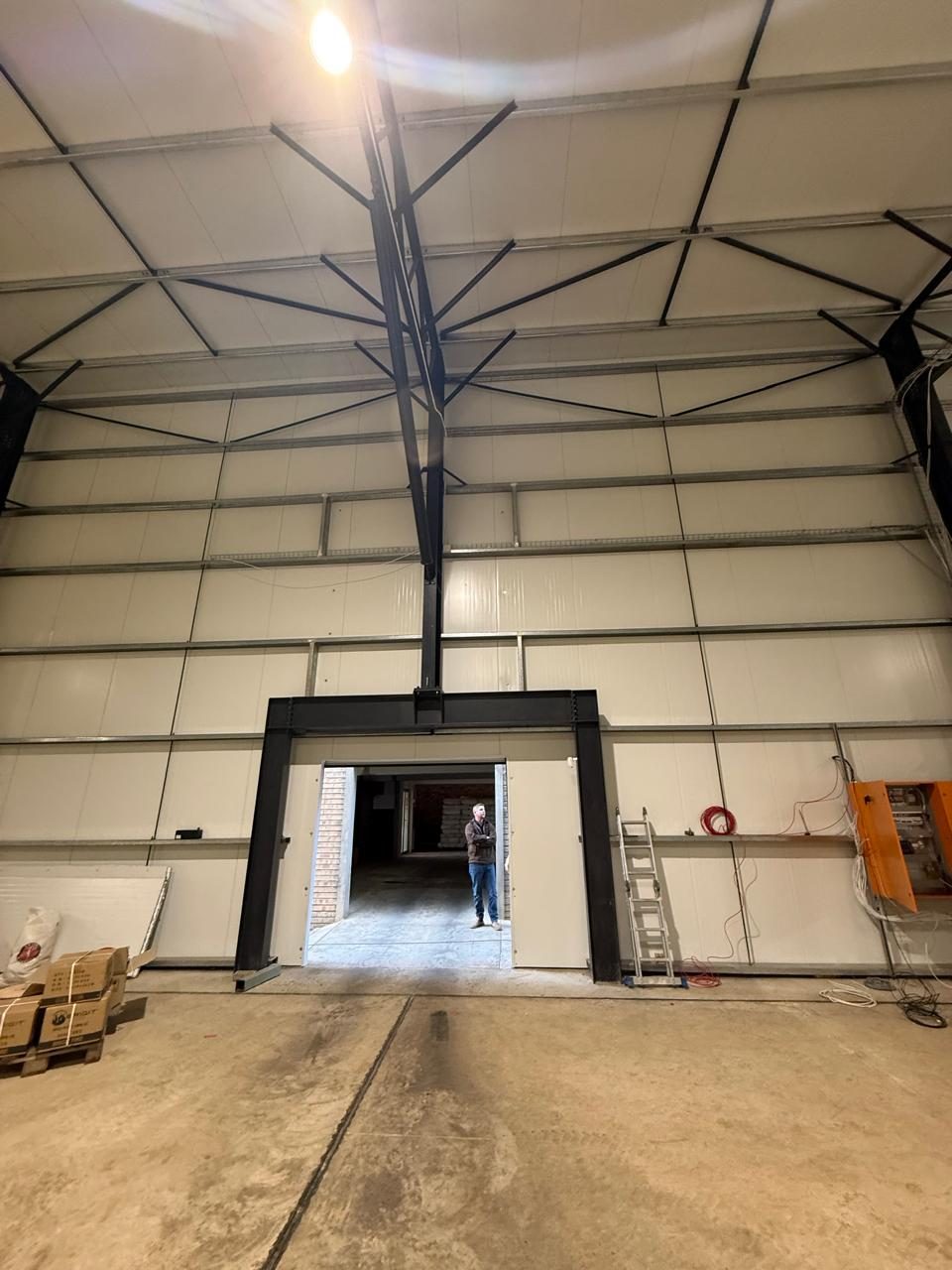 The junction to squint at. The door opening is trimmed against the portal column and the panel is cut and closed at the reveal; the horizontal tongue-and-groove joints run through the wall above without a break. The offcut boards stacked at the left show the sandwich on edge.