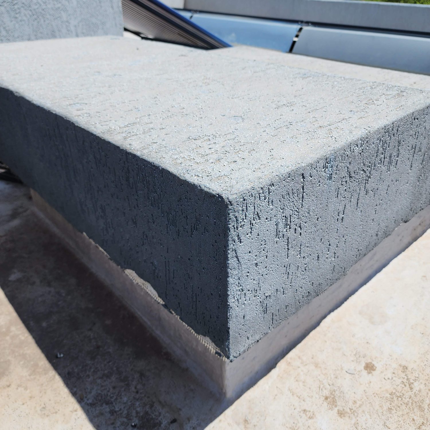 The parapet cap. The render is taken over the top of the parapet and down the face as one continuous skin, and the arris is mitred sharp enough to cast a hard shadow. Bottom left, the glass-fibre mesh is still exposed in the basecoat where the topcoat stops — that mesh is what holds the corner.