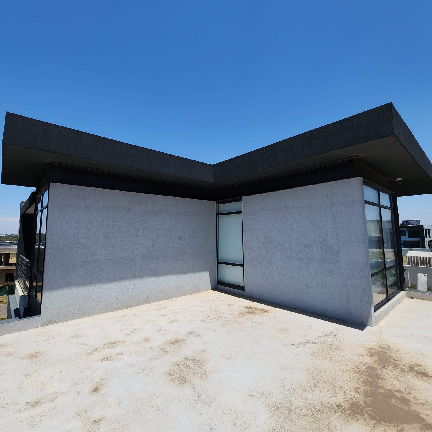 Roof-deck walls meeting the charcoal parapet band. The change from pale wall to dark band is a colour change, not a material change — the same system takes both — and the render carries around the external corner without a bead line breaking the texture.