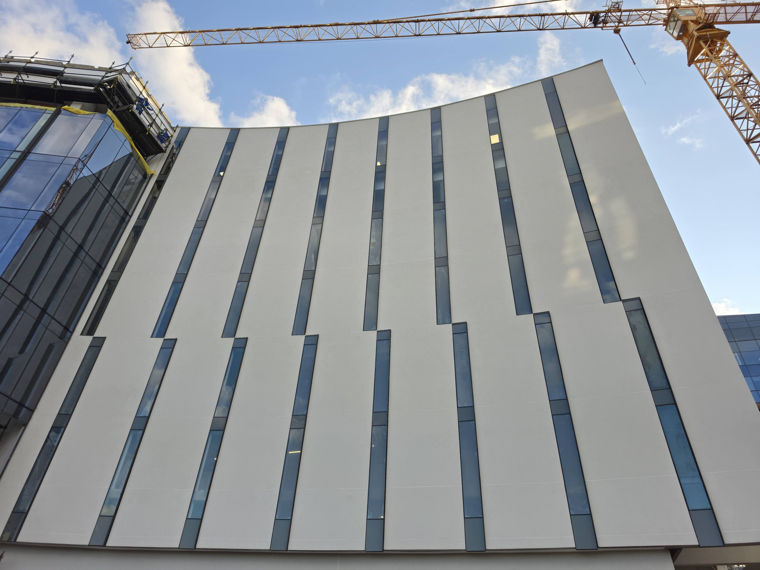 The swept elevation seen from below. The wall curves in both plan and roofline, and the white surface carries round the curve unbroken between the slot windows.