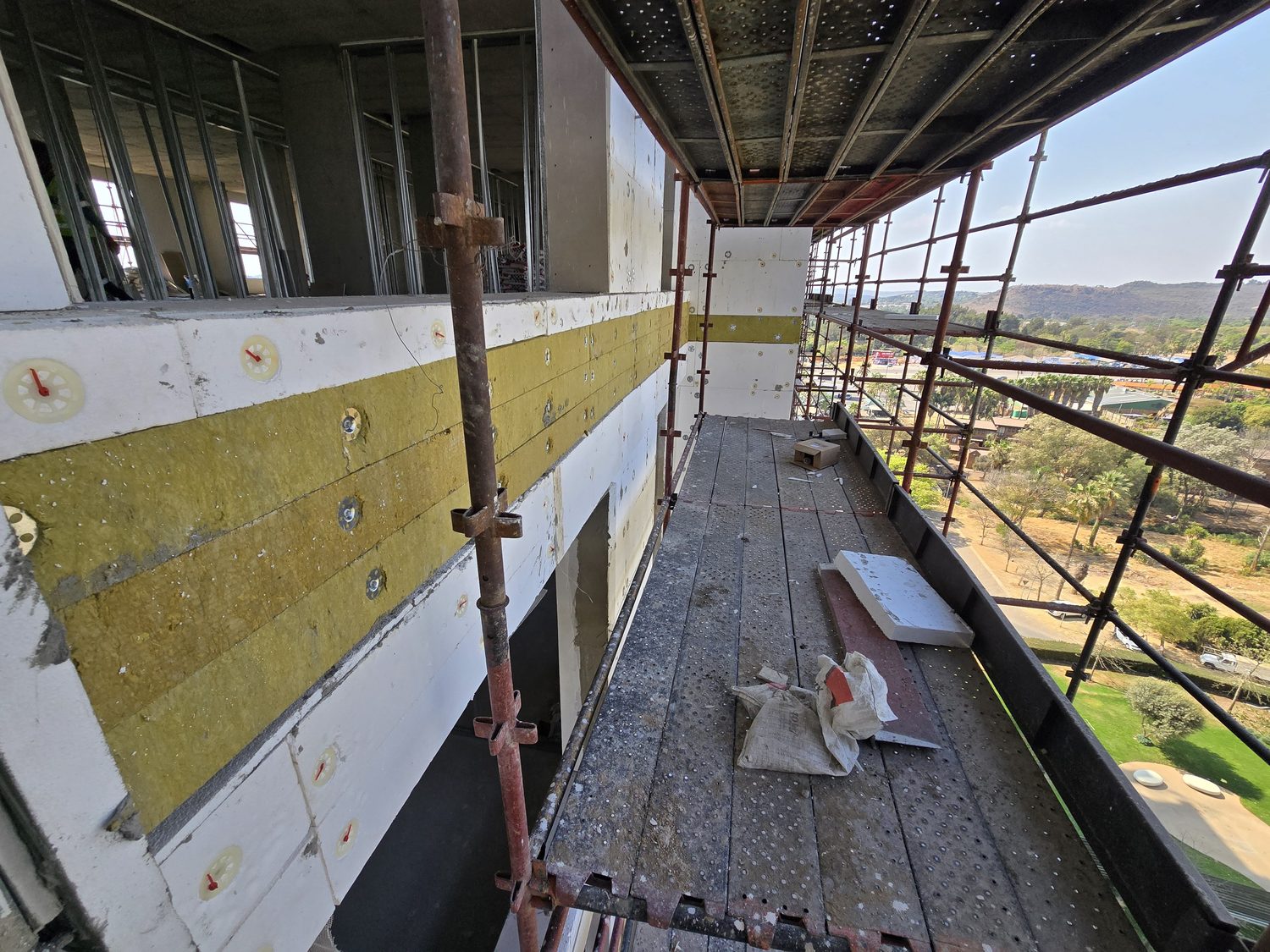 The build-up before render. White EPS board fixed back with washer-and-pin anchors, and a band of mineral wool set into the insulation at every floor line — the horizontal fire break at each slab edge. This is what the specifier should look for on a high-rise EIFS: the insulation layer is deliberately interrupted, not continuous.