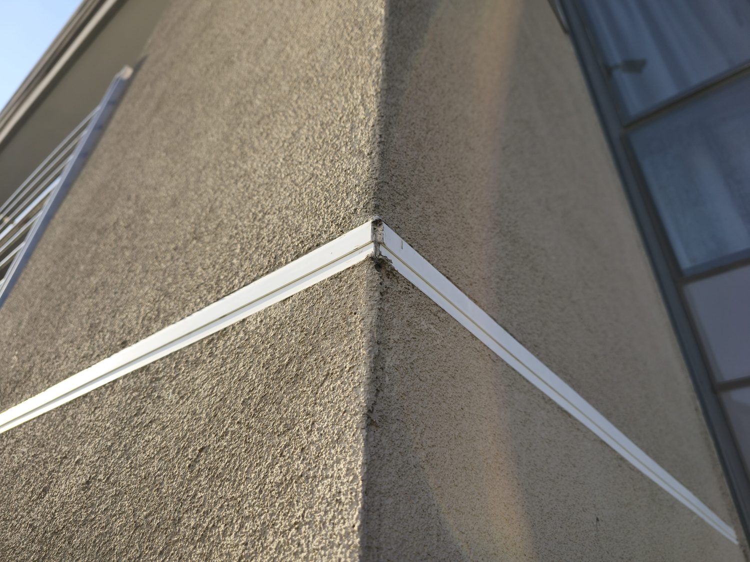 External corner, finished. The Terracoat grain runs unbroken around the arris and terminates against a bead, giving a straight, sharp edge and a defined stop. No feathered wet edge and no cracked corner.