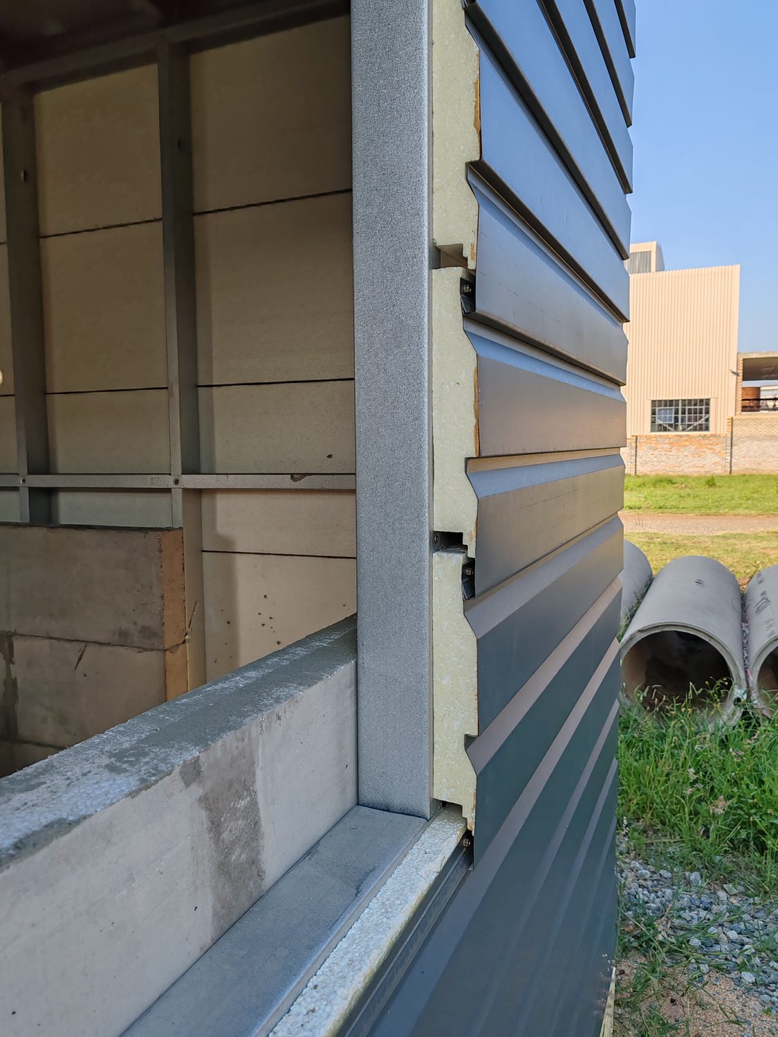 The detail to squint at. Cladding cut back at the opening shows the entire stack at once — steel stud, EPS board behind, and the black concealed clips screwed through the board into the frame. Each board hooks over the one below; nothing penetrates the visible face.