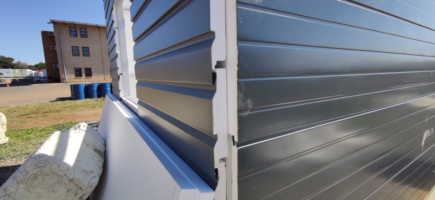The external corner. The weatherboard returns past the arris onto the adjacent panel and the EPS substrate thickness is visible in the joint — proof that LiteClad is the 0.5 mm skin and the insulation is the board behind it, not the metal.