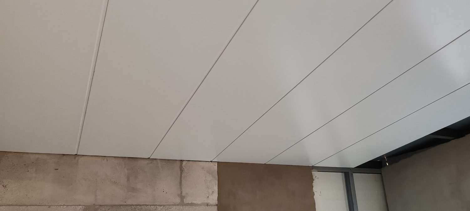 The same steel overhead. Flat LiteClad panels used as the finished ceiling, fixed direct off the structure — the joint lines and the slight oil-canning in raking light are what a light-gauge flat panel actually looks like as a ceiling.