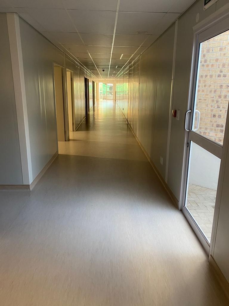 The finished corridor: two pale walls whose only lines are the panel joints about a metre apart, doors set flush in the panel line, a suspended ceiling above and sheet vinyl underfoot.