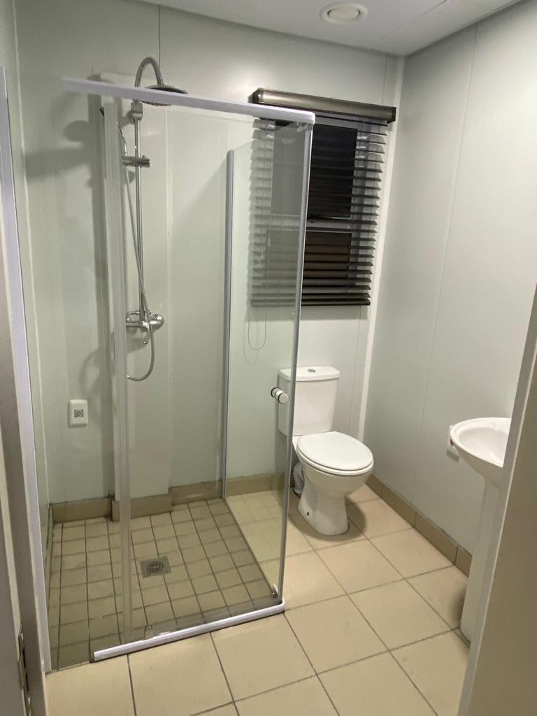 An en-suite shower room where the walls are the panel face itself. The shower enclosure, WC and basin are fixed to it, a window is cut through it, and the tiling stops at the floor.