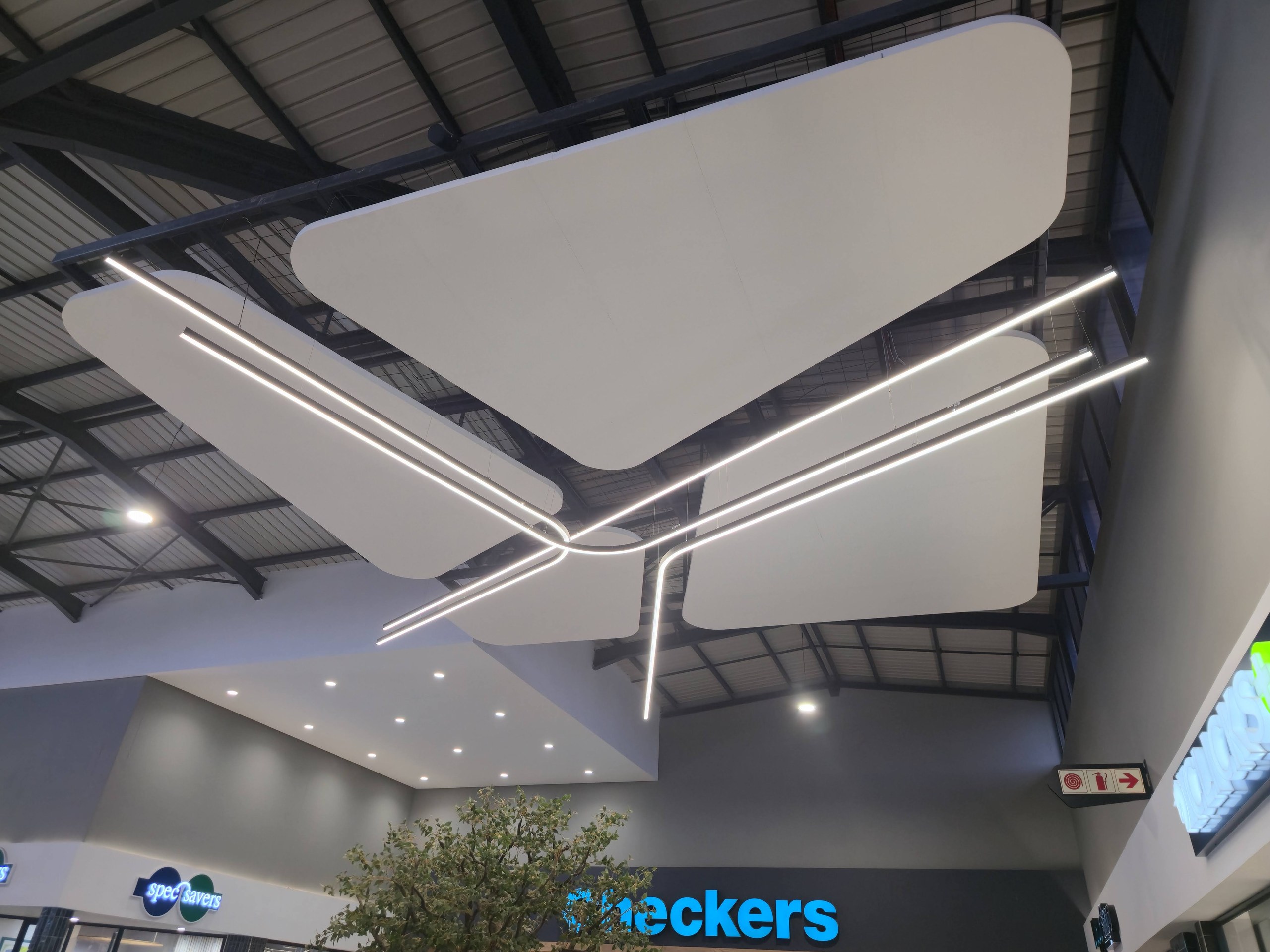 Large shapes over the concourse with thin linear light lines running beneath and alongside them. At this size the smooth coated underside and the rounded bullnose edge are clearly readable.