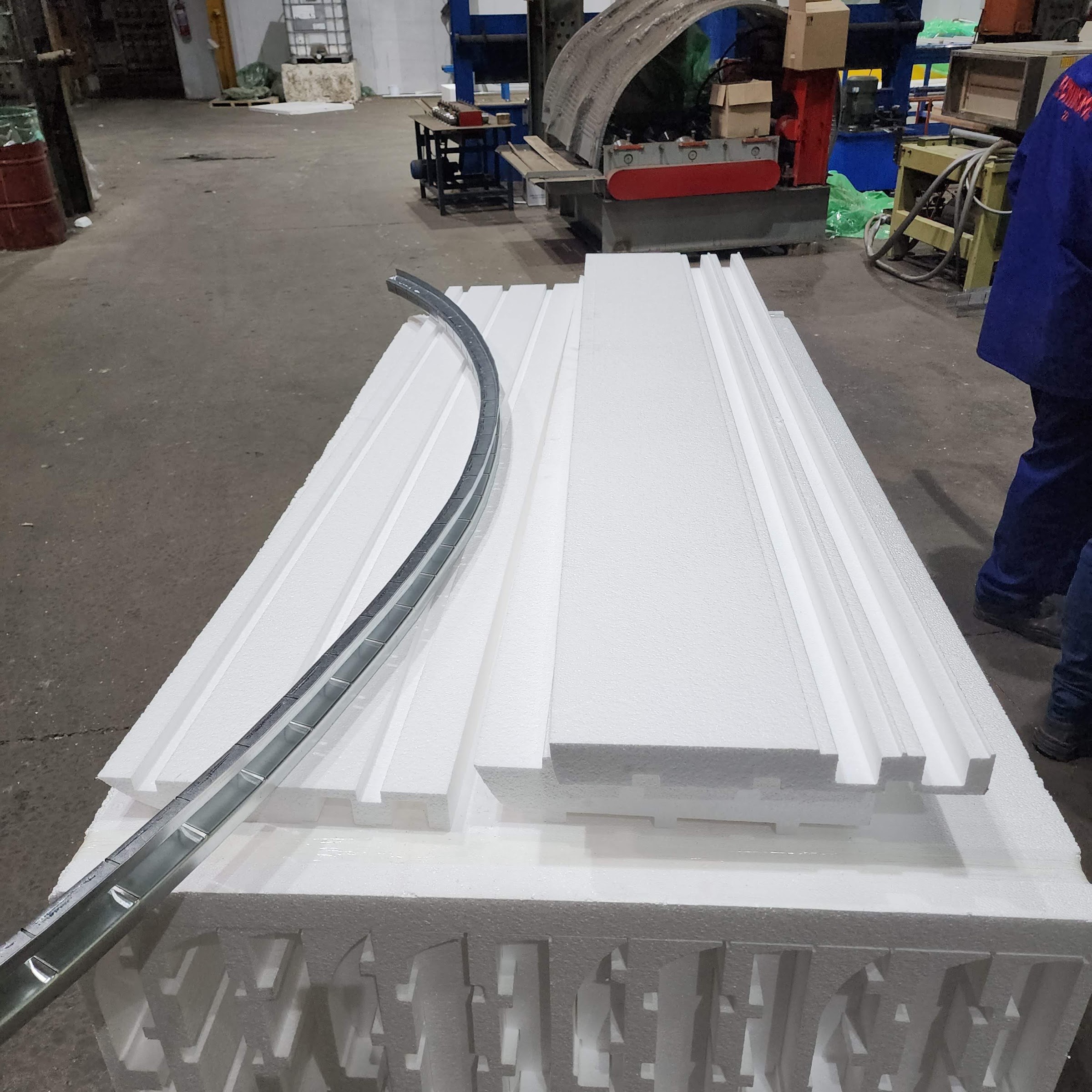 Cut moulding sections stacked on the block they came out of - the block face carries the negative of several complete profiles - with a notched galvanised channel bent to a curve lying across them