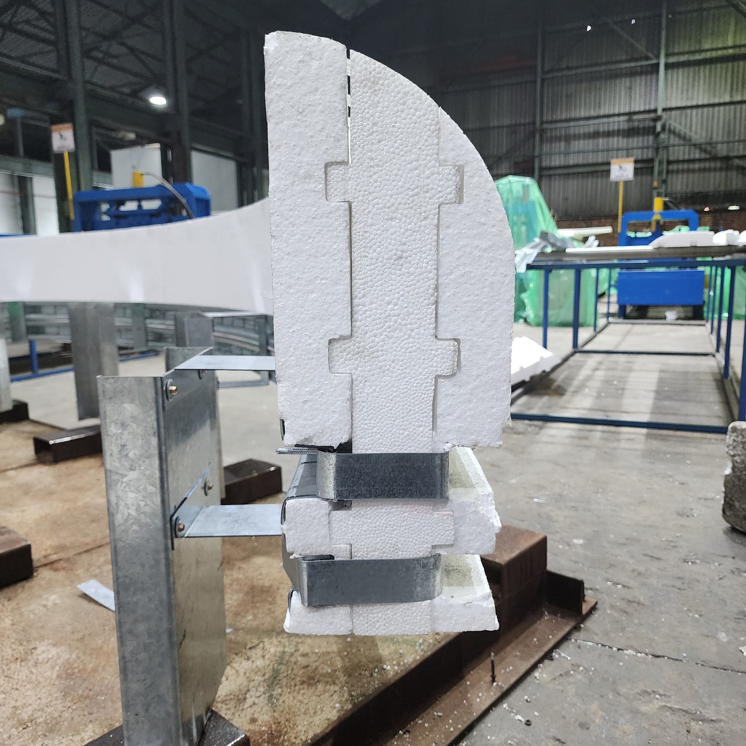 End view on the factory jig - the interlocking stepped joint face between two moulding segments, the foam rebated down onto galvanised channels, and the channels carried on a bracket bolted to an upright