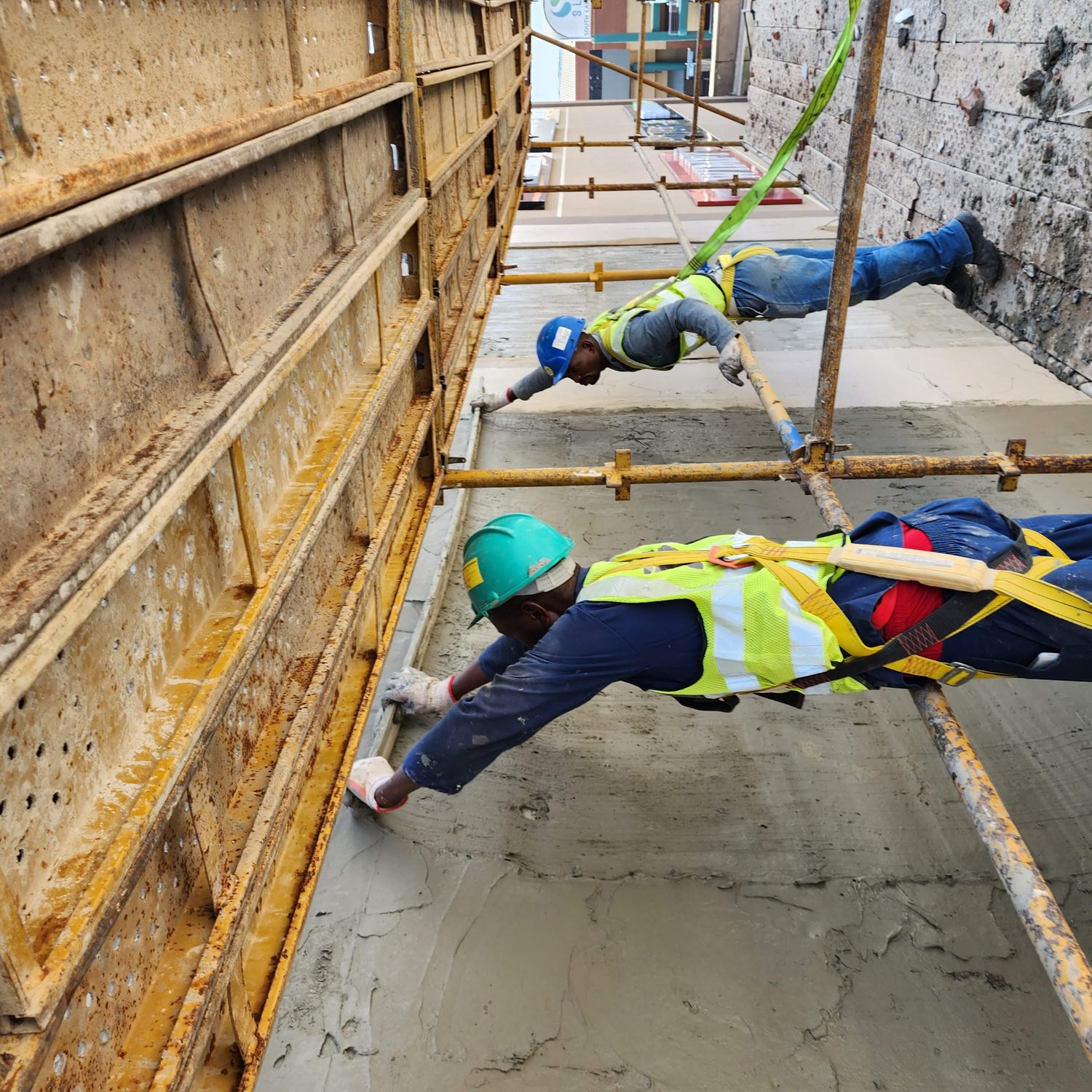 Basecoat being floated onto the board on the parapet lift. This is the coat the Terramesh is embedded into while it is still wet — the crack-control layer, applied off the same scaffold, over a live centre.