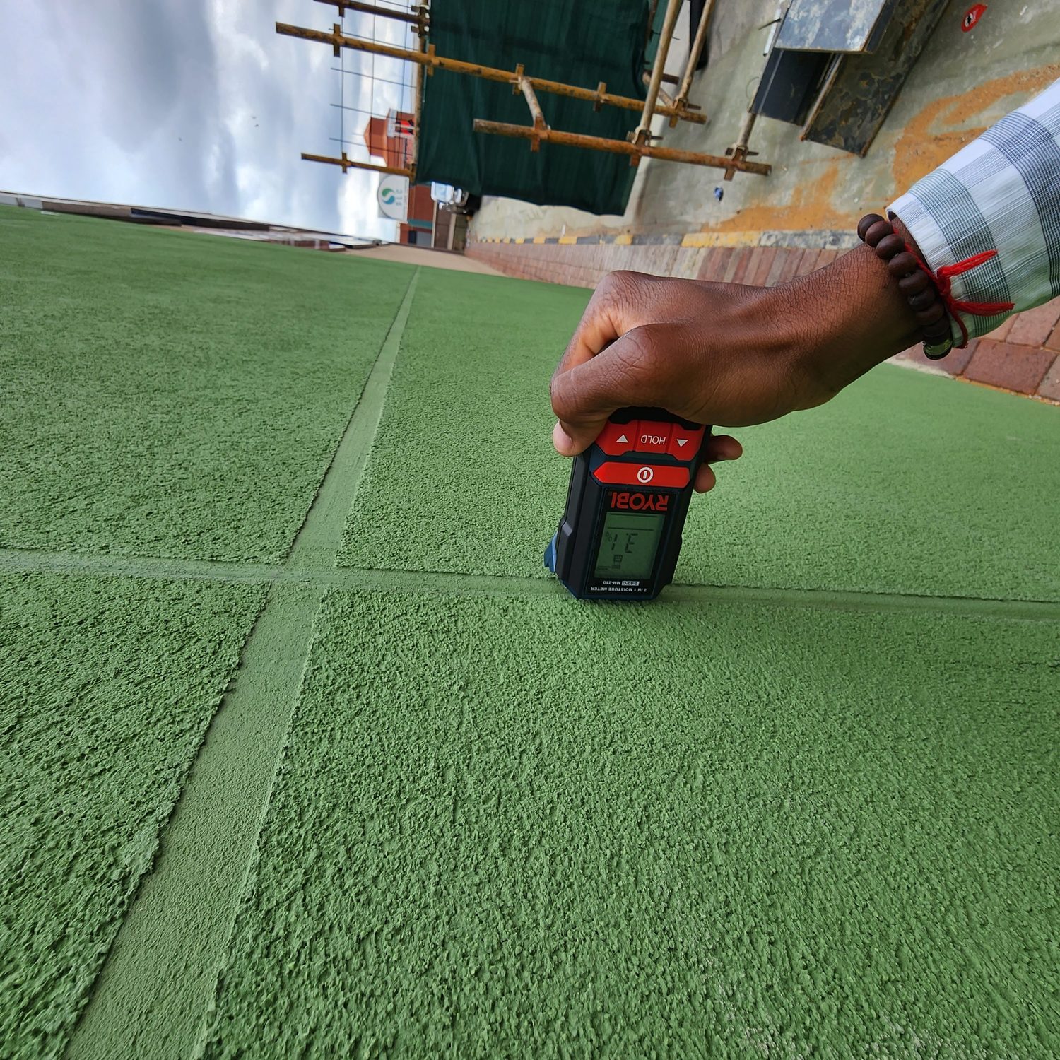 Close on the cured topcoat in raking light: the grain of the texture, and the false joint struck sharp and straight across a large flat field. A moisture reading being taken on finished work.