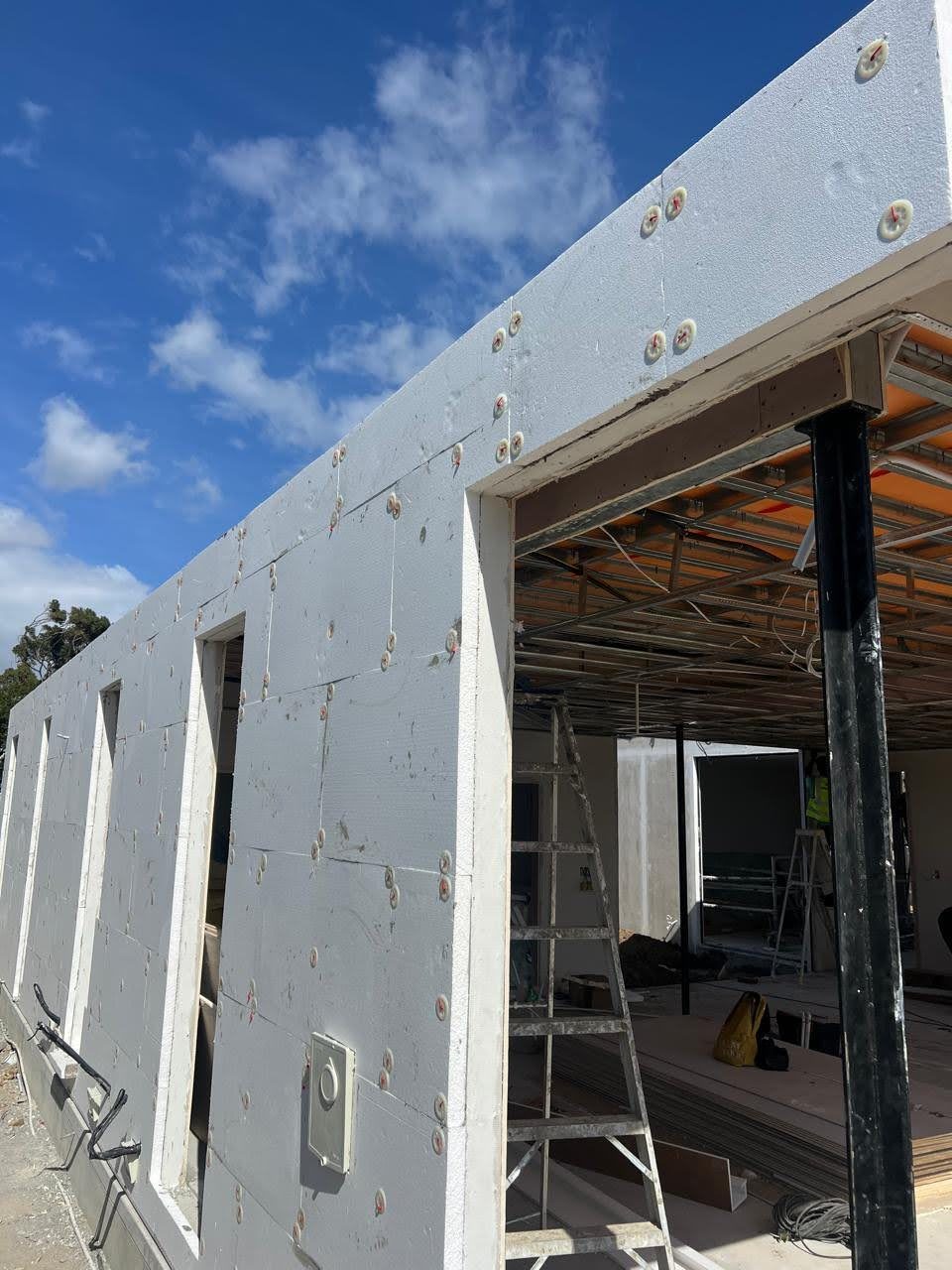 The same kind of wall before render: EPS board carried up the face and turned over the roof edge, mechanically fixed with washer plates over a sheathed frame. The insulation runs past the structure rather than between it — look at where the board meets the steel and the ceiling grid inside.