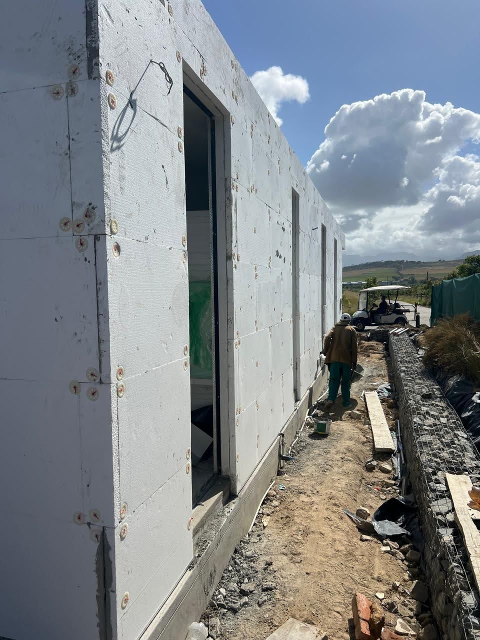 The long elevation, boards on and reveals returned into every opening, stopped on a base trim clear of the ground. Reveals and the base of the wall are the two junctions where an EIFS facade usually fails — both are formed here before a drop of render is on.