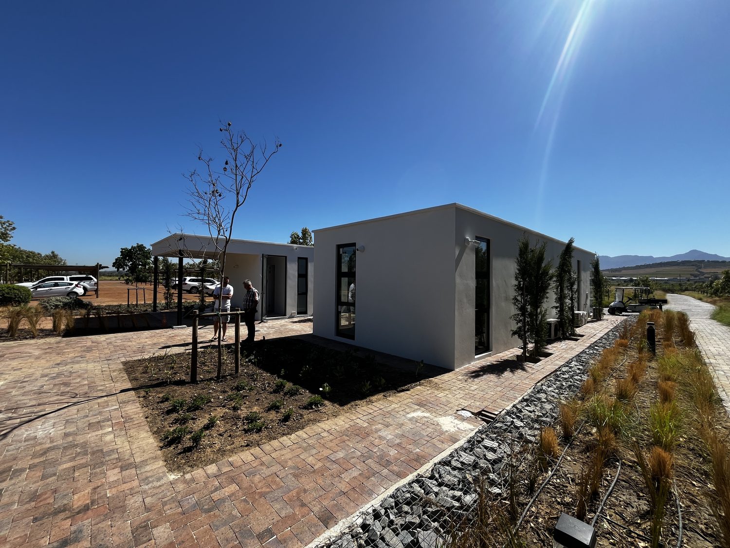 Context. The units sit in open vineyard, full sun on the white elevations, mountains behind. The render skin is doing the weathering on a light framed building — there is no masonry backing it up.
