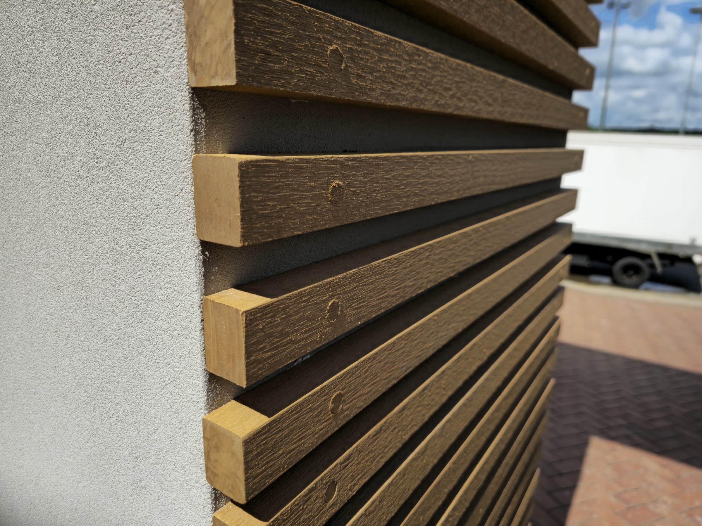 The finished fine-grained textured coating meeting the timber batten cladding, with the shadow gap and the plugged batten fixings alongside.