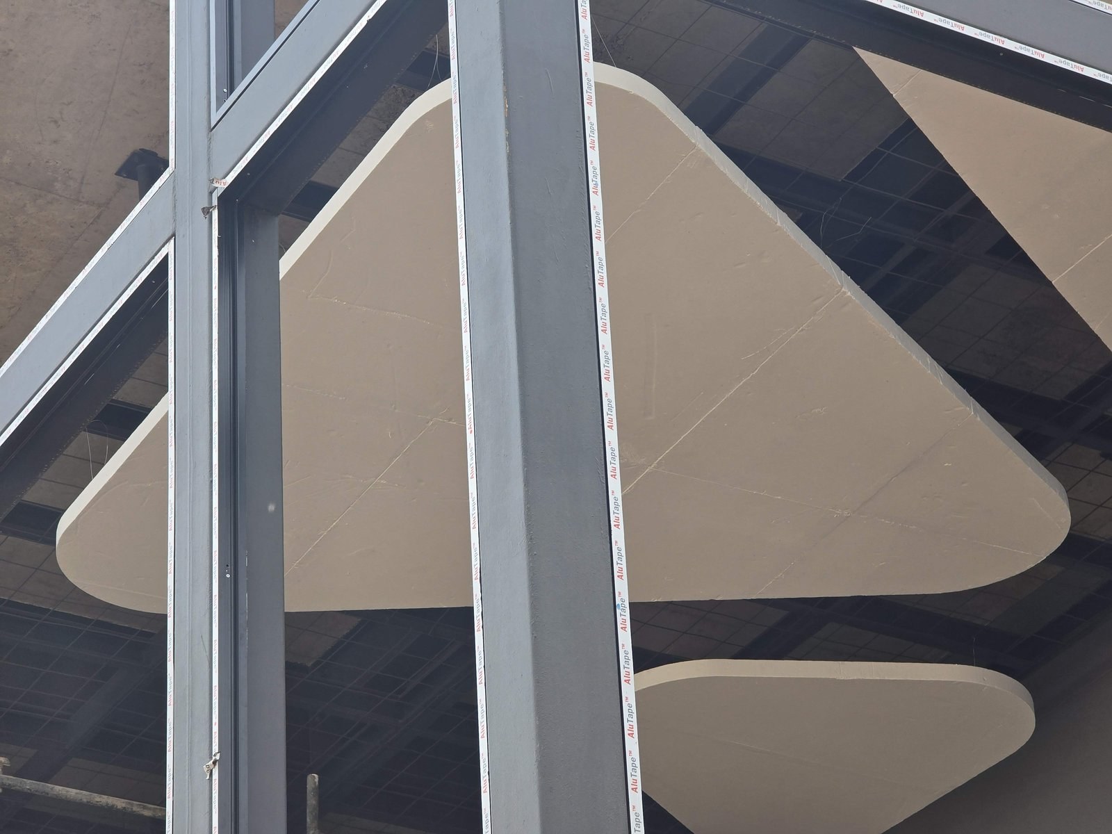 Close-up of two of the suspended shapes past a steel column: thick square edges, rounded corners and a smooth coated face, with faint joint lines across the panel.