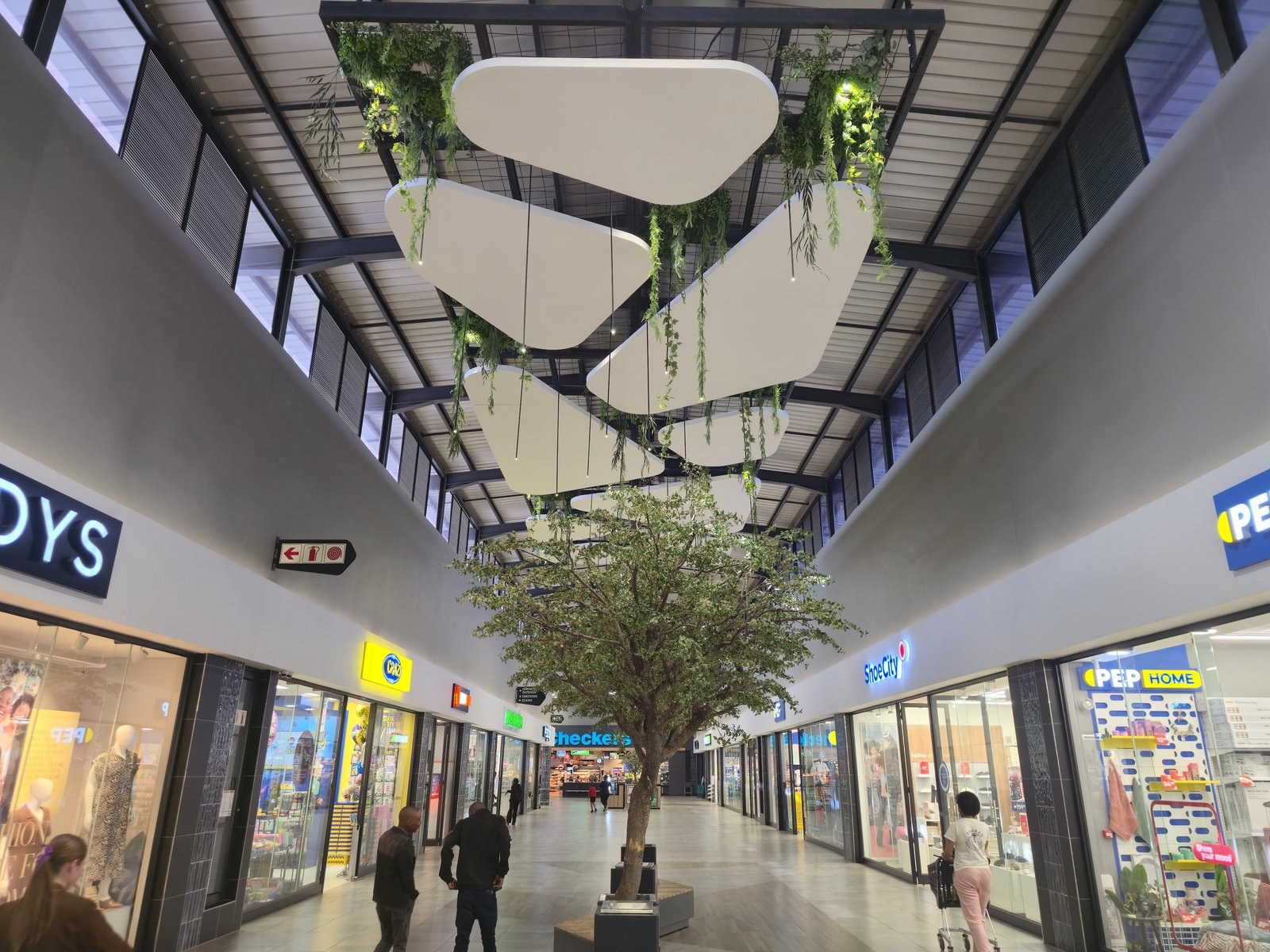 The shapes in use: flat white profiles hung at staggered heights above a mall walkway, between the steel frame and the shopfronts below.