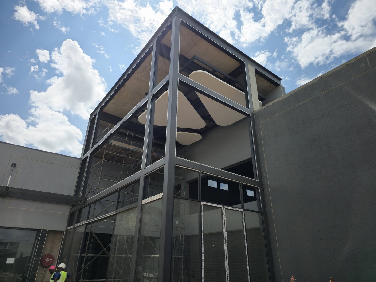 The same shapes seen from outside during construction - hanging inside the glazed entrance tower, with scaffolding still up behind the glass.