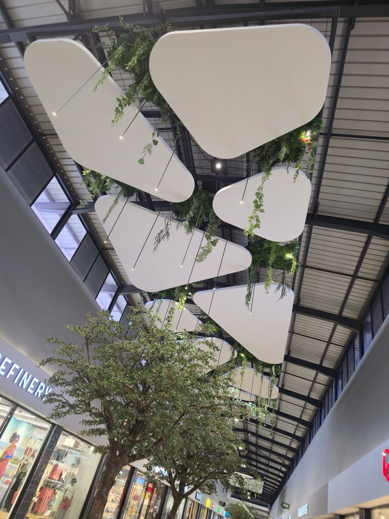 Rounded-triangle EPS ceiling shapes with trailing artificial greenery, viewed looking up above The Refinery store at Riverstone Mall.