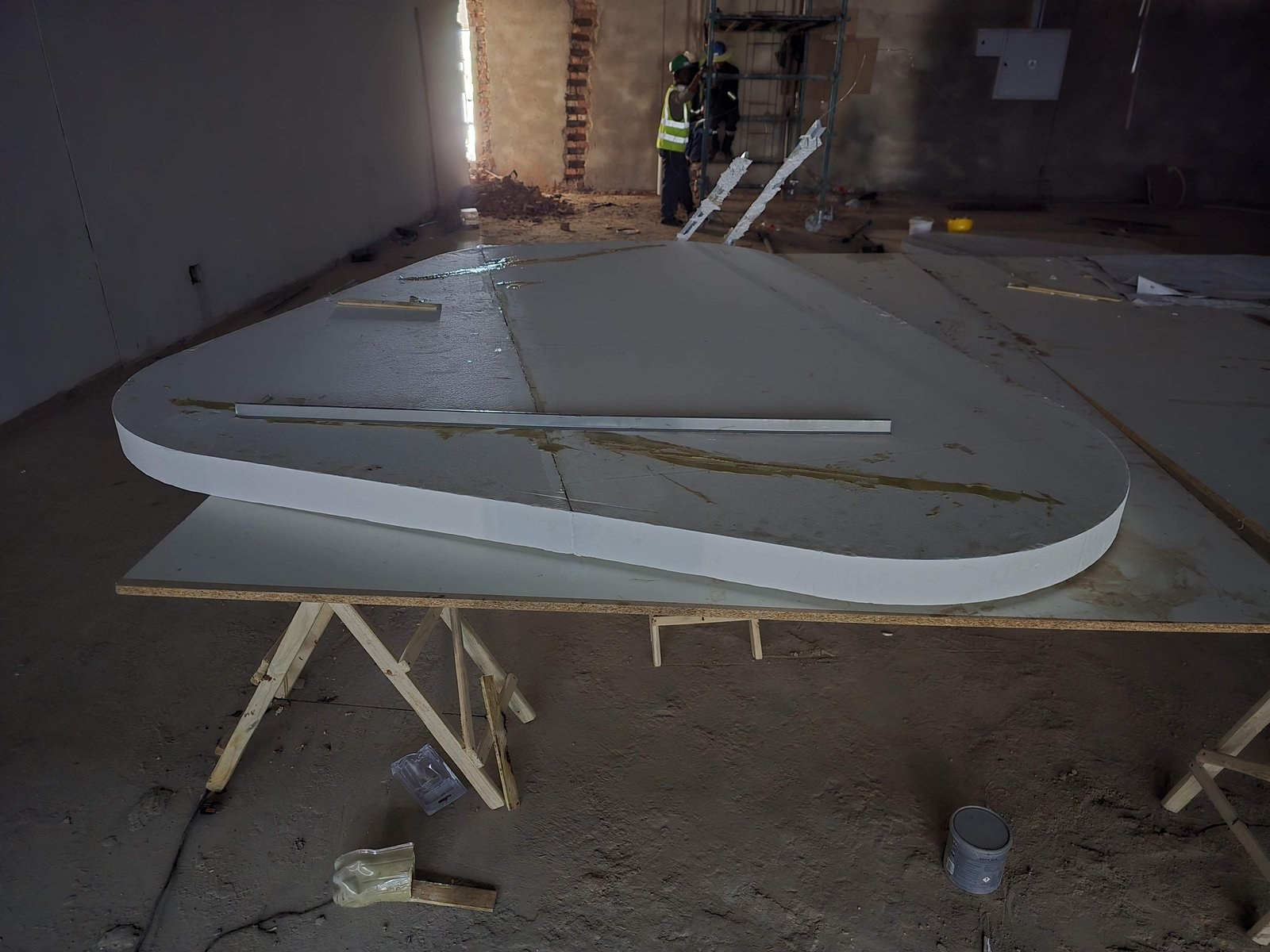 Rounded EPS shape resting on a sawhorse trestle table on site, with construction workers visible in the background.