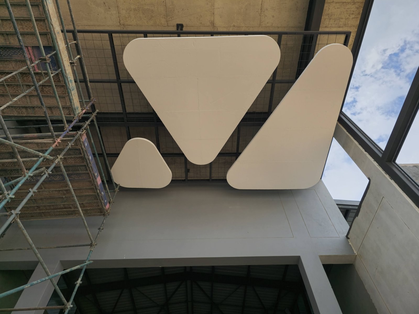 Unpainted triangular EPS shapes fixed to overhead steel mesh framing during installation, scaffolding alongside.