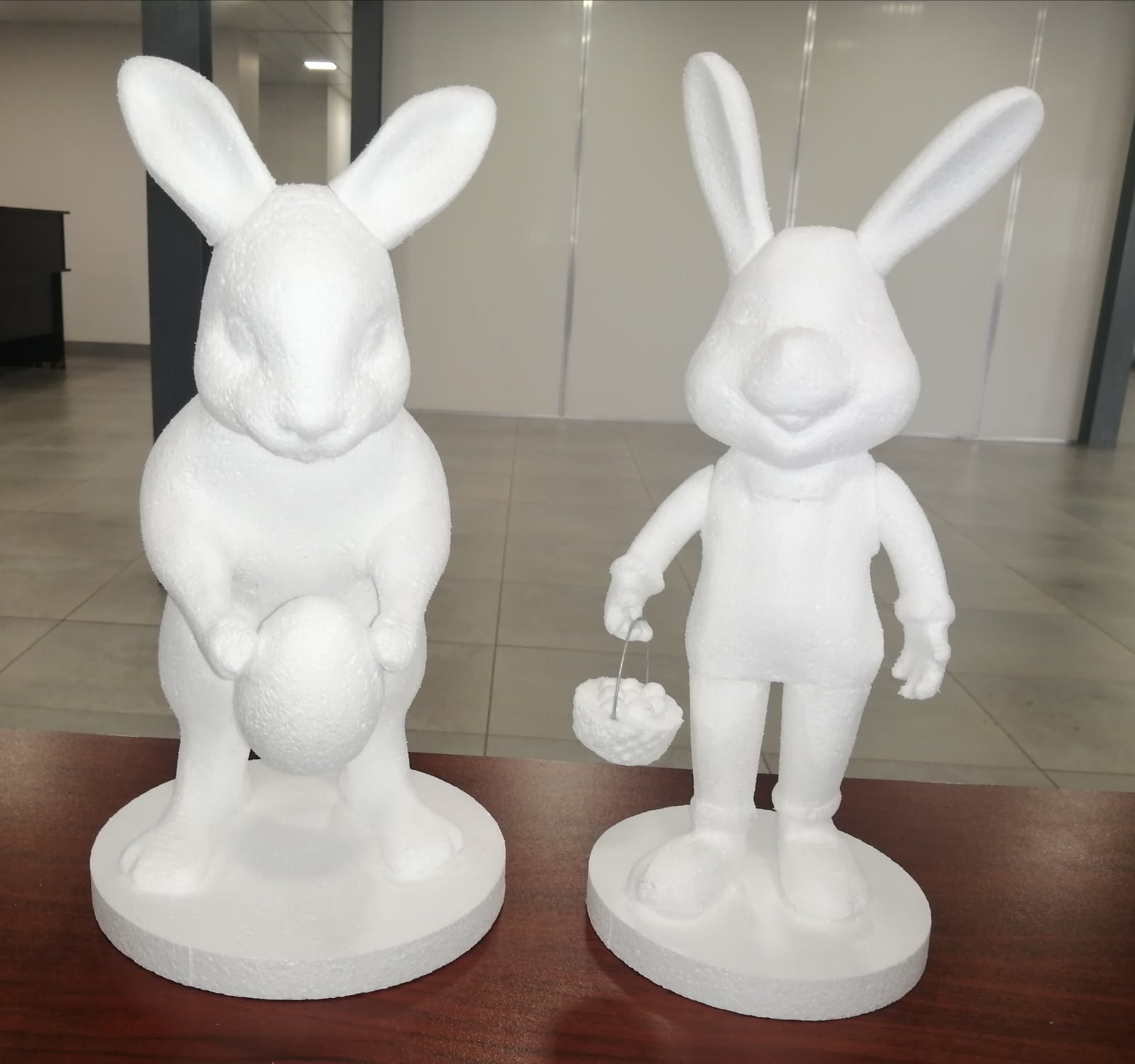 Two rabbit figures milled in EPS on round bases - one crouching with an egg, one standing in clothes carrying a basket of eggs. Both are shown raw off the machine, with the foam bead texture and soft facial modelling still unfinished.
