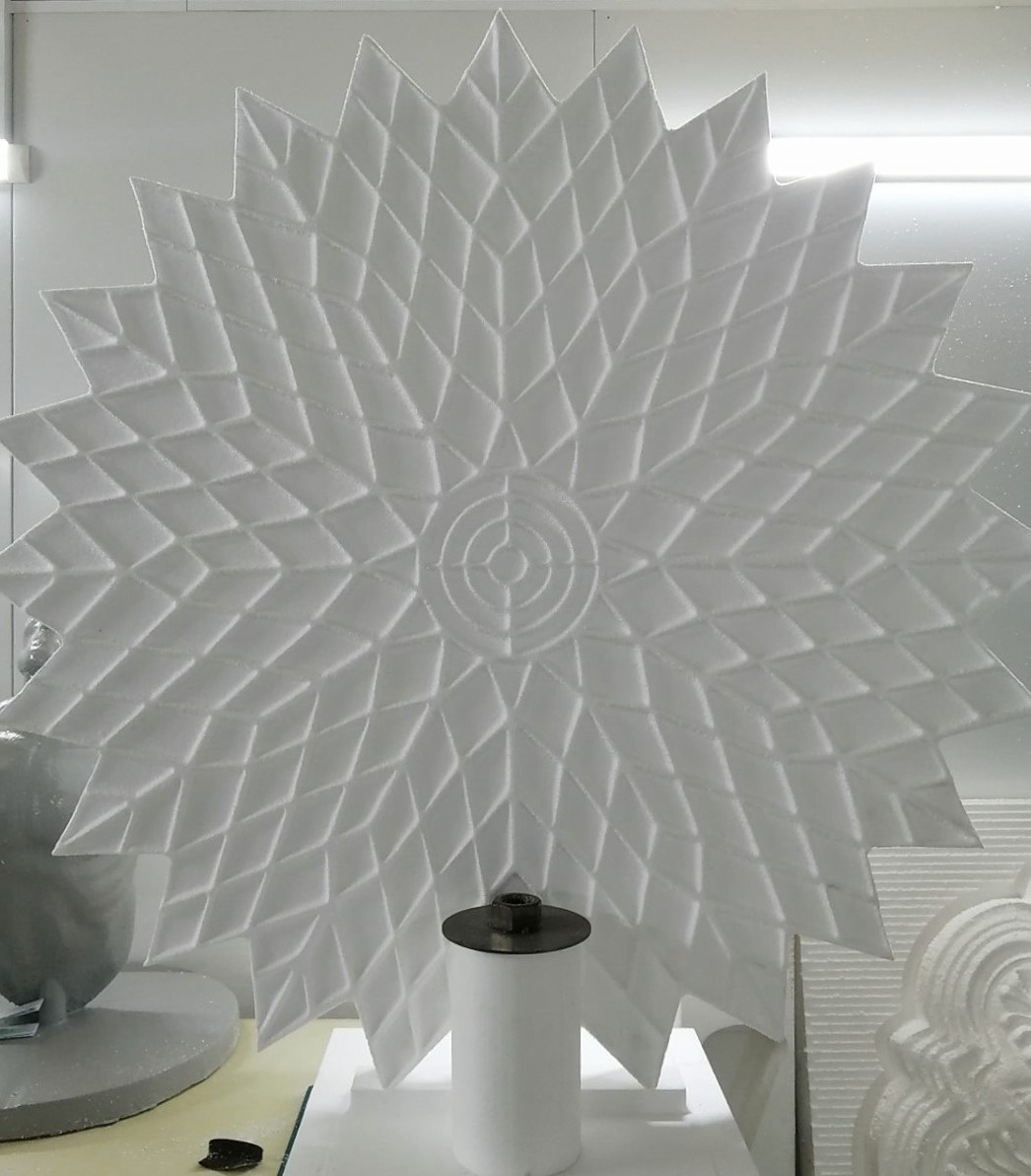 A star rosette milled in EPS - concentric rings of sloped diamond facets radiating from a turned centre, with a spiked outer edge. Stood up in the workshop next to other milled pieces, including a grey-coated bird sculpture at left.