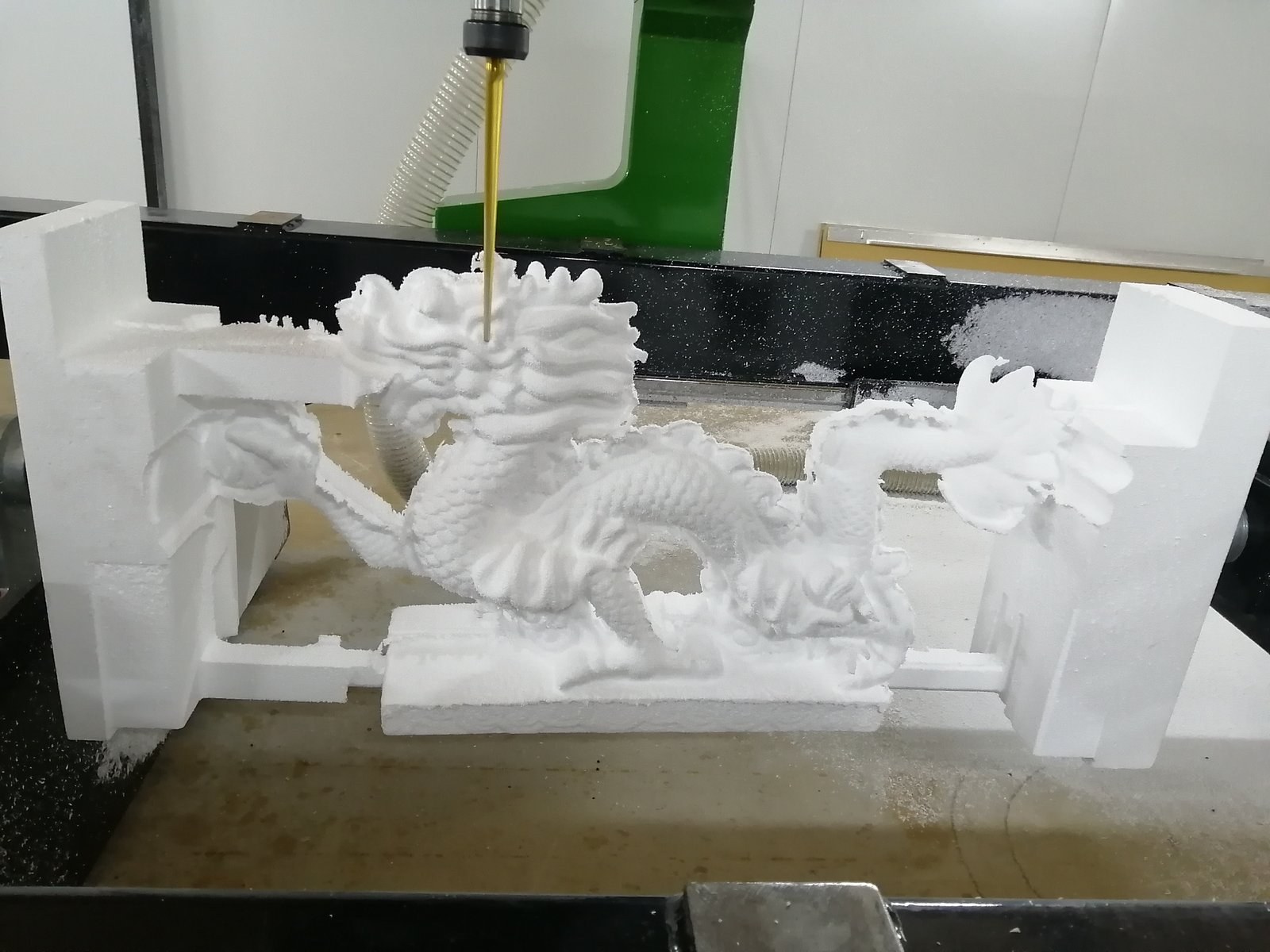 CNC router mid-cut on a dragon sculpture, spindle still bearing down on the EPS block