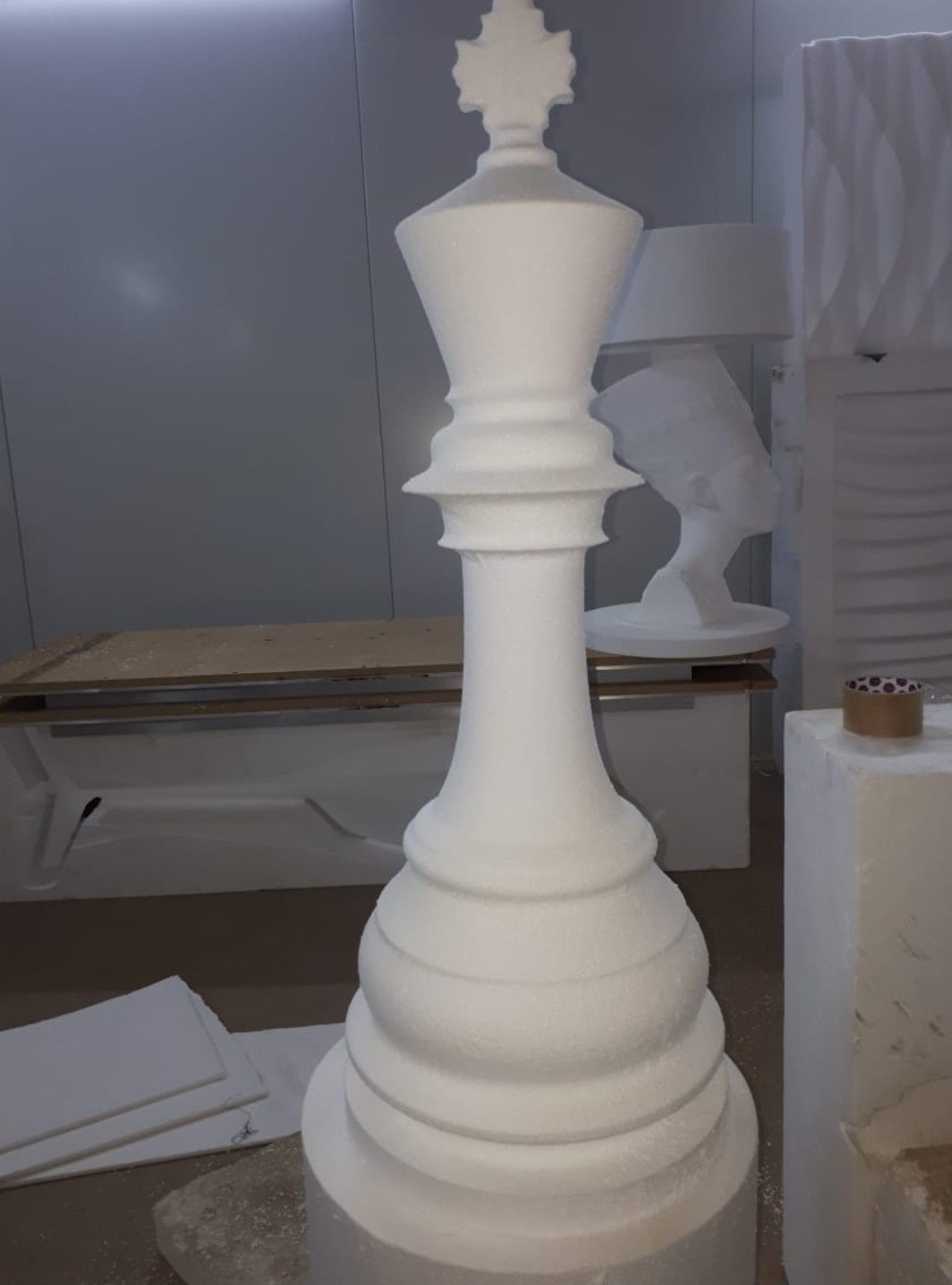 Oversized chess king piece carved from EPS, other carved pieces visible in the workshop behind it