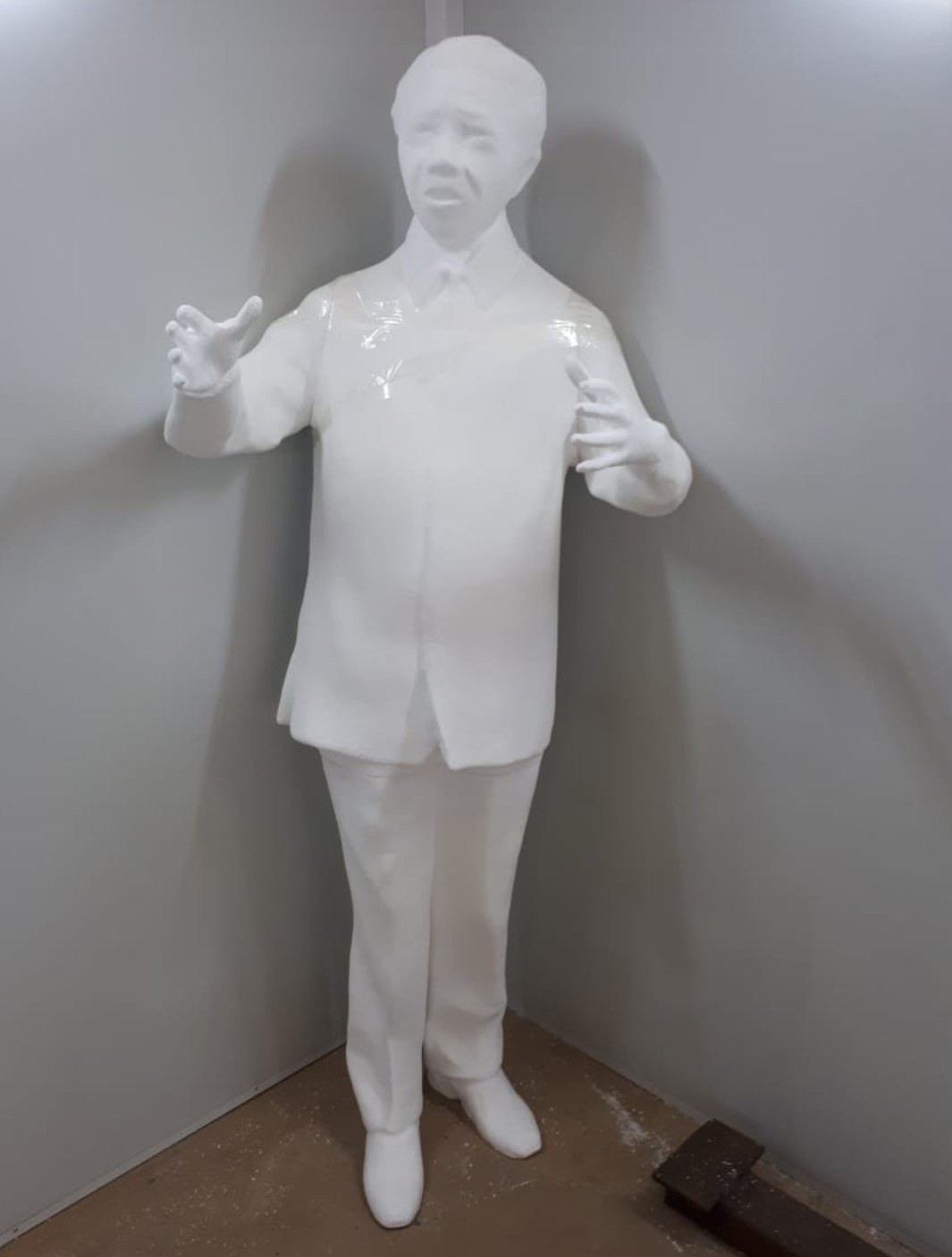 Life-size human figure carved from EPS, arms raised, plastic film over the torso, standing in a workshop corner