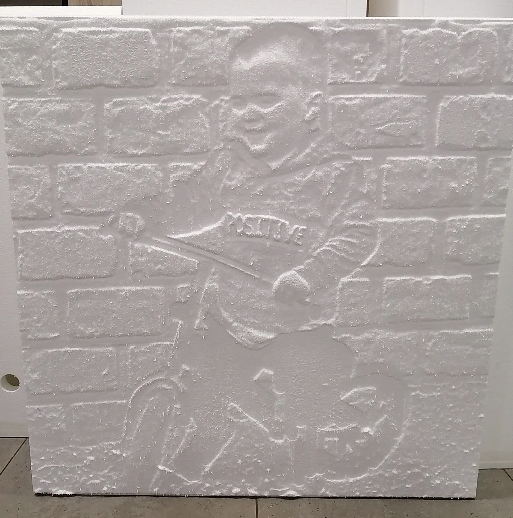 Photo of a child on a bicycle turned into a 3D relief carving, set against a milled brick-pattern background