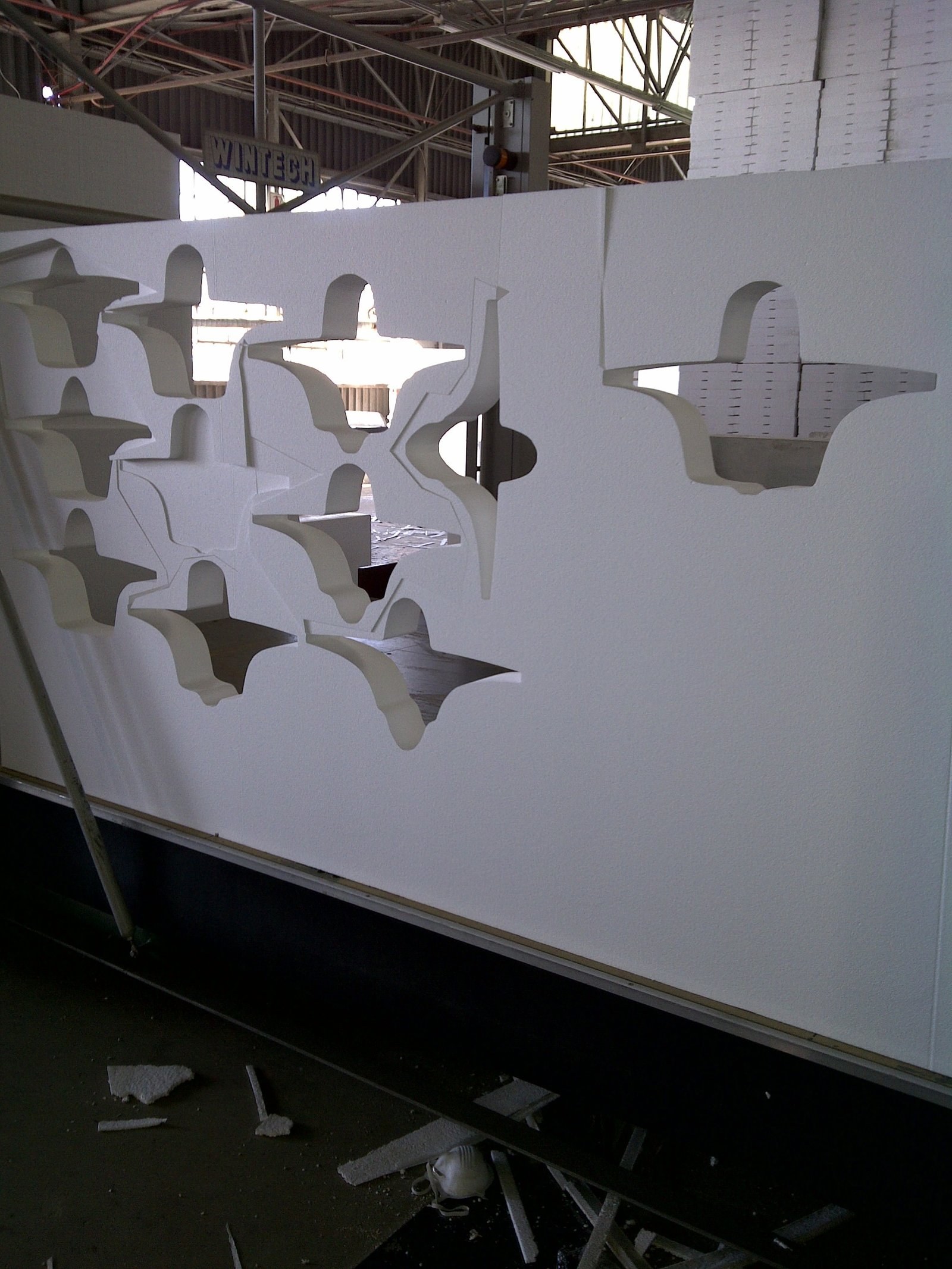 Block of EPS with rows of bracket-shaped pieces CNC-cut, some already removed and others still nested in the panel