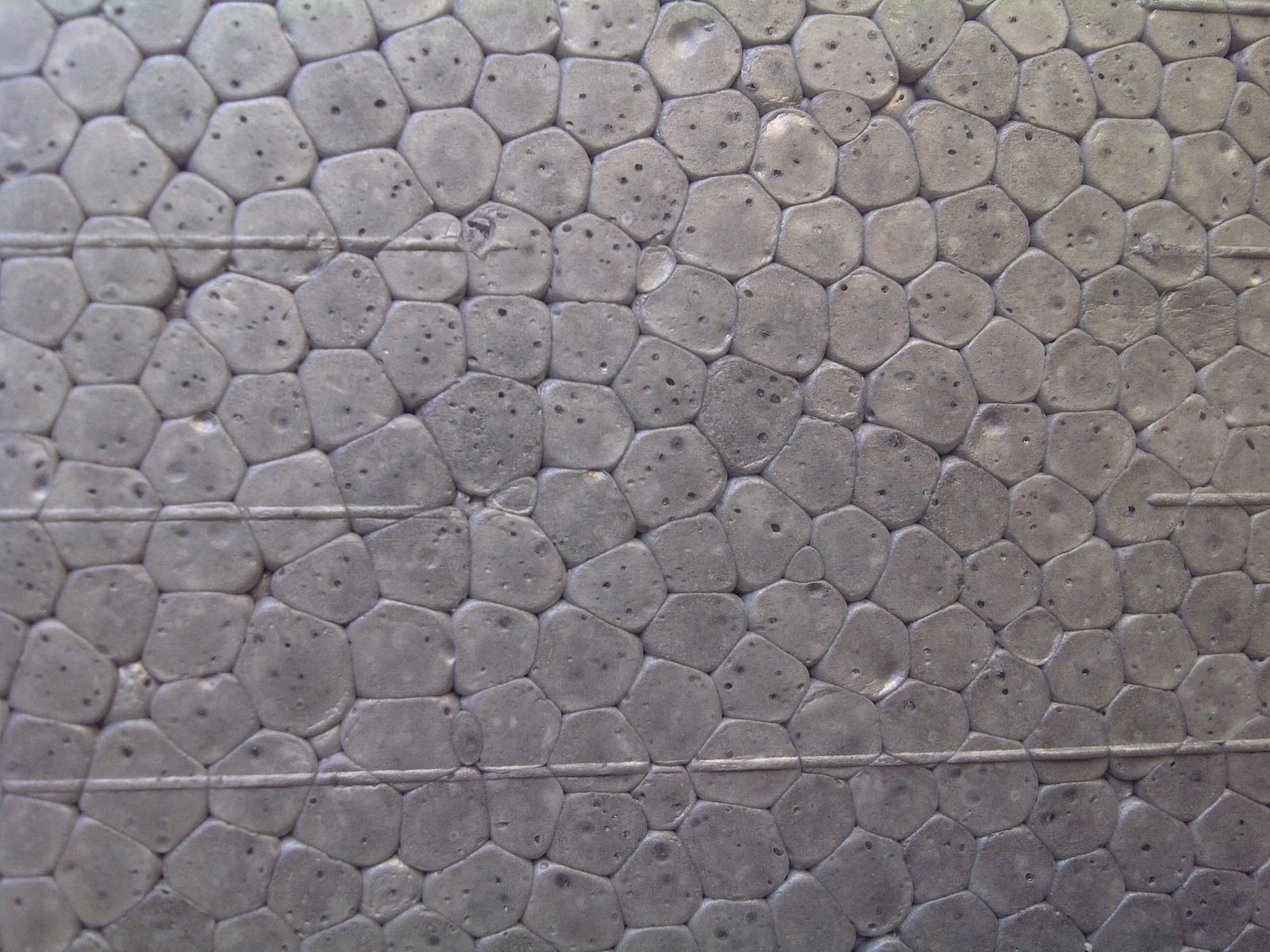 Macro of the cut face of a grey EPS board: individual expanded beads fused into one another, with faint straight hot-wire cut lines crossing the surface.
