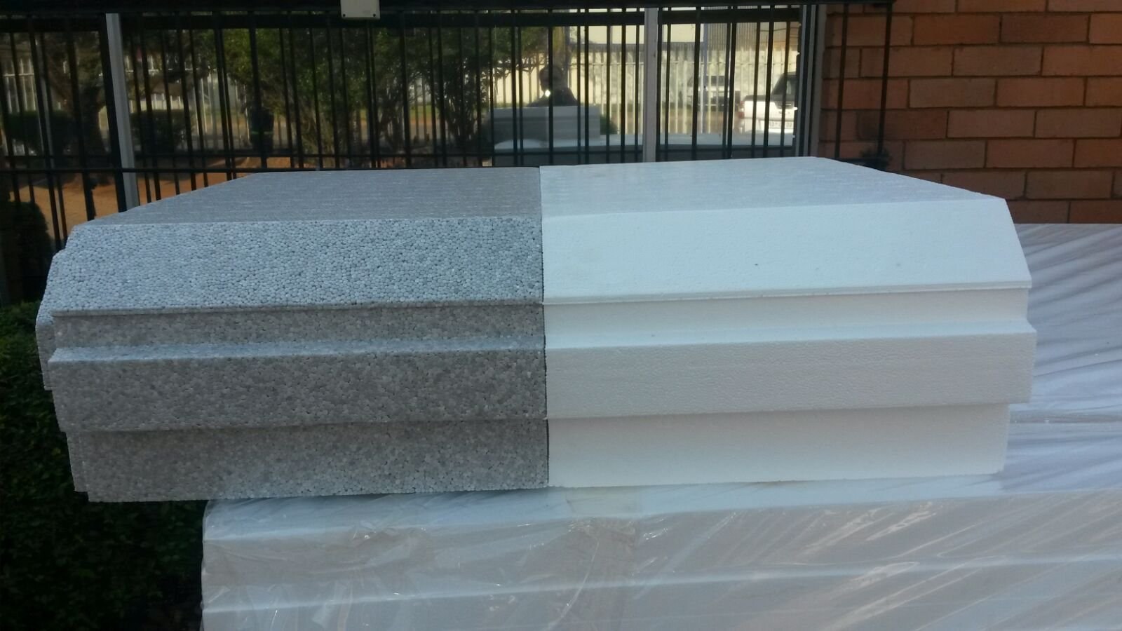 Grey and white EPS boards stacked together on a wrapped bundle outside the factory, the stepped shiplap edge visible along the front of each board.