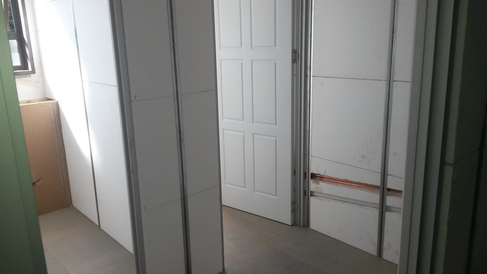 Corridor of EPS panel walls with a copper pipe run let into the board face, door fitted at the end