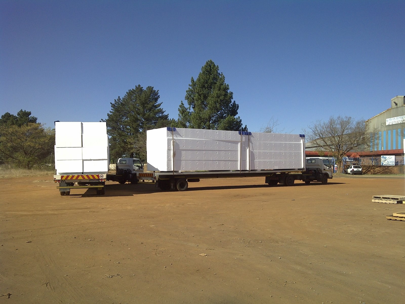 Two flatbed trucks loaded with EPS panel stacks in the yard