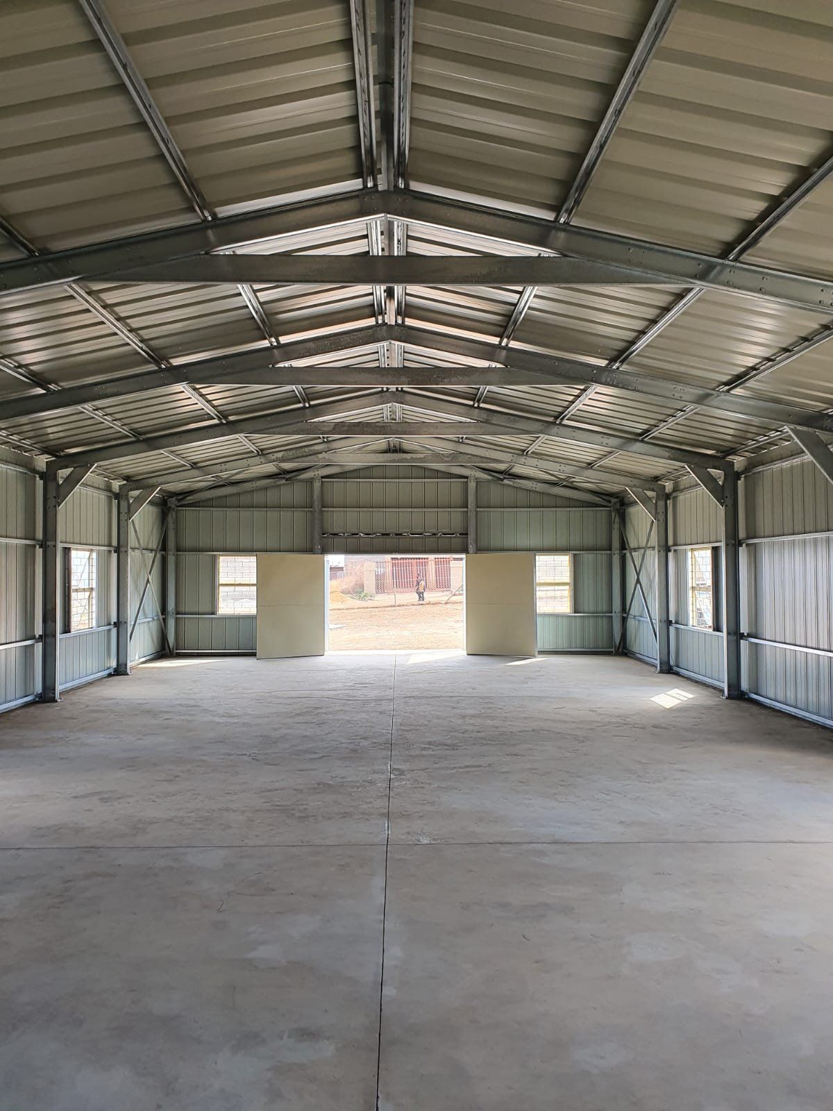 Cold-formed steel portal frame with purlins being sheeted over as roofing is installed