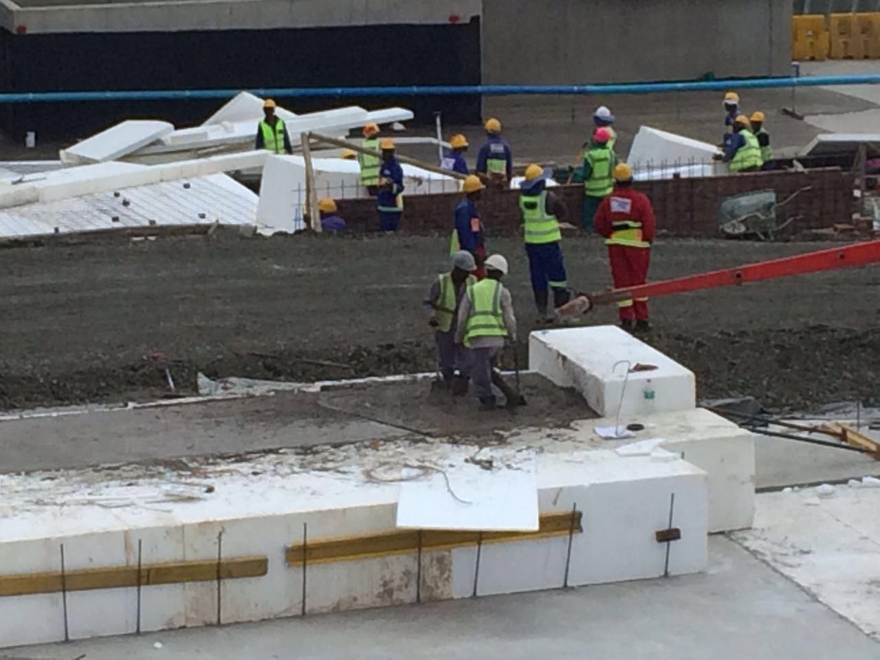 A run of EPS blocks laid end-to-end on the levelled platform, with steel bars and a batten set across the top course. Site crew and offcuts around the working face.