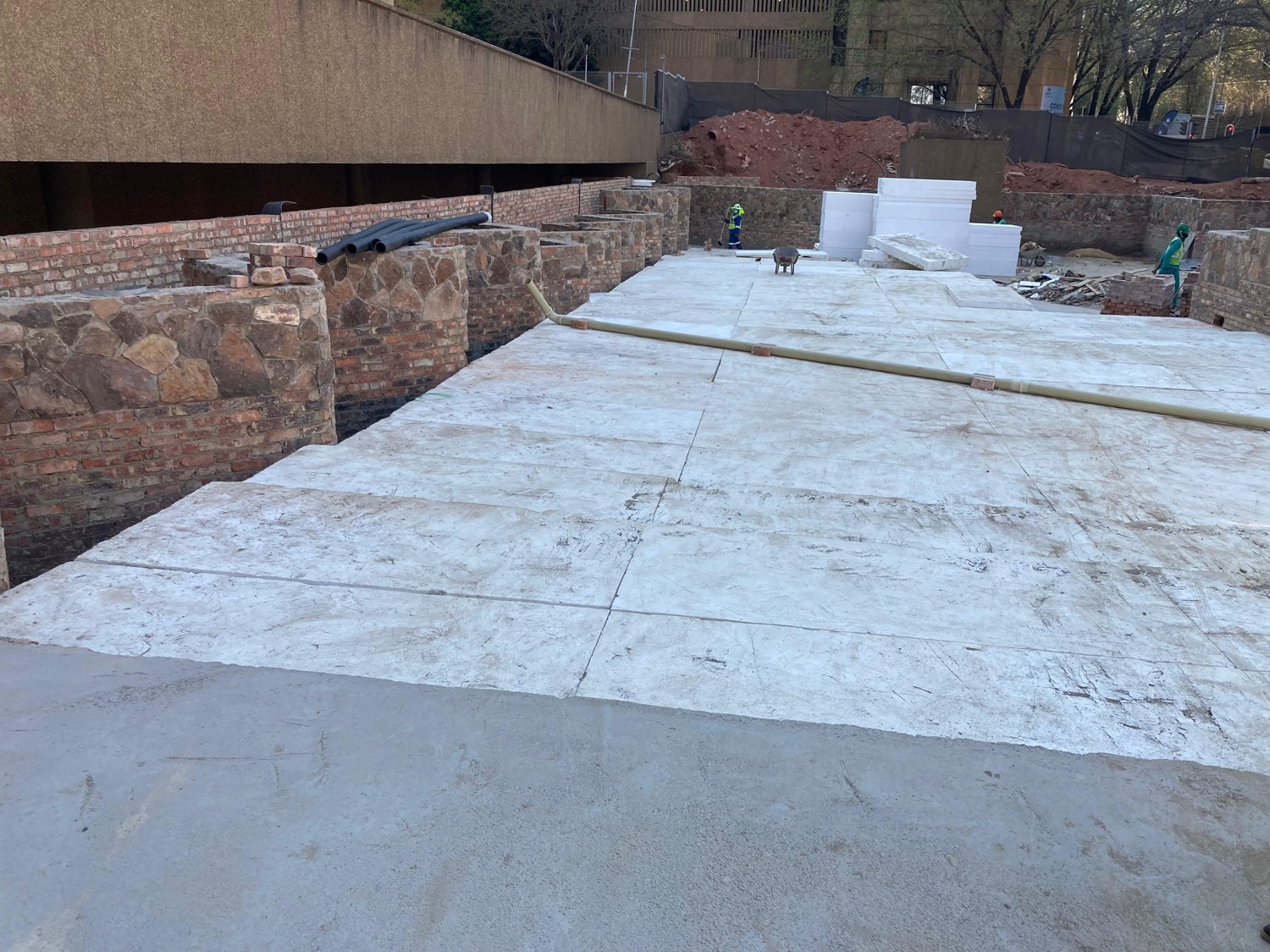 EPS blocks laid tight and level to form a continuous fill platform between the stone and brick retaining walls; the trafficked top faces are scuffed grey with site dirt. Further blocks stacked at the far end.
