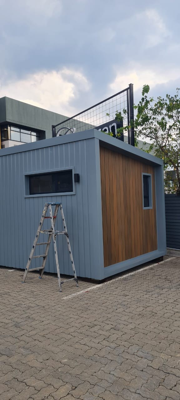 Modular unit clad in grey vertical-rib profiled steel sheeting, with a vertical timber-slat end panel. Photographed on site during fit-out.