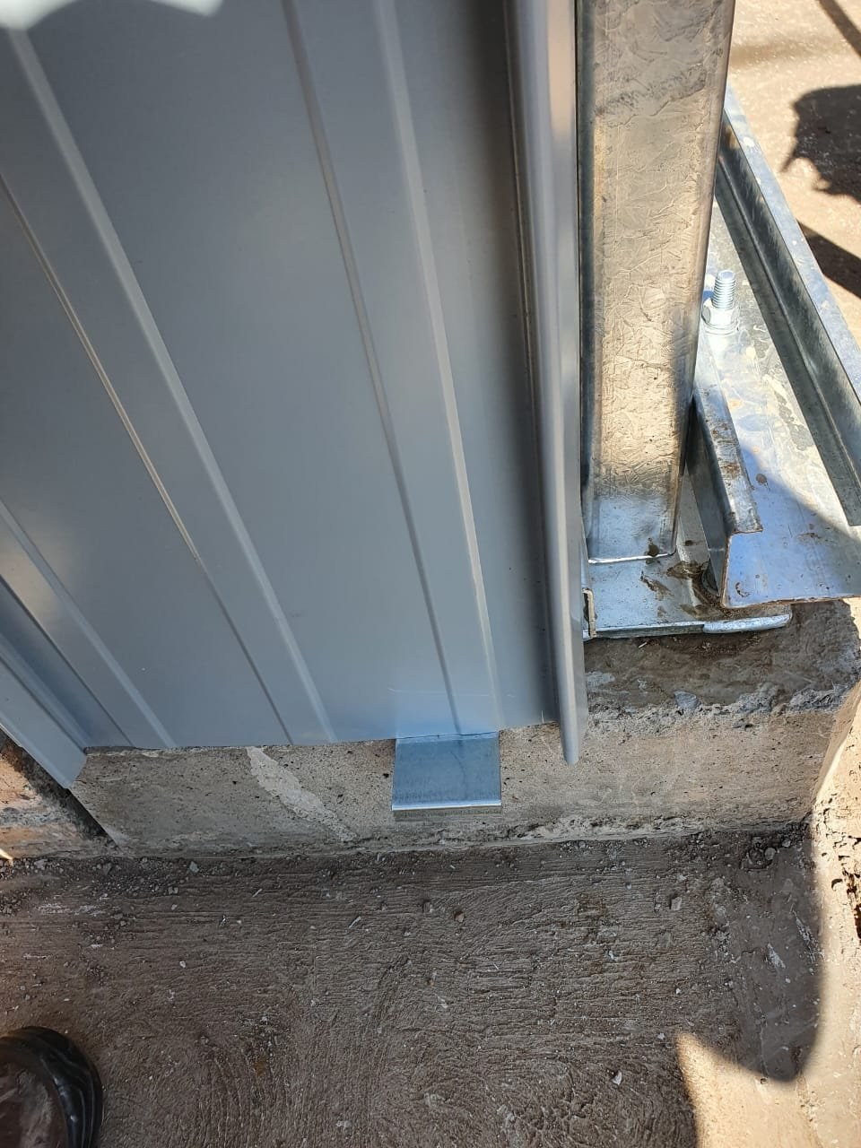 Close-up of a steel wall panel base fixed with a flashing bracket to a concrete plinth