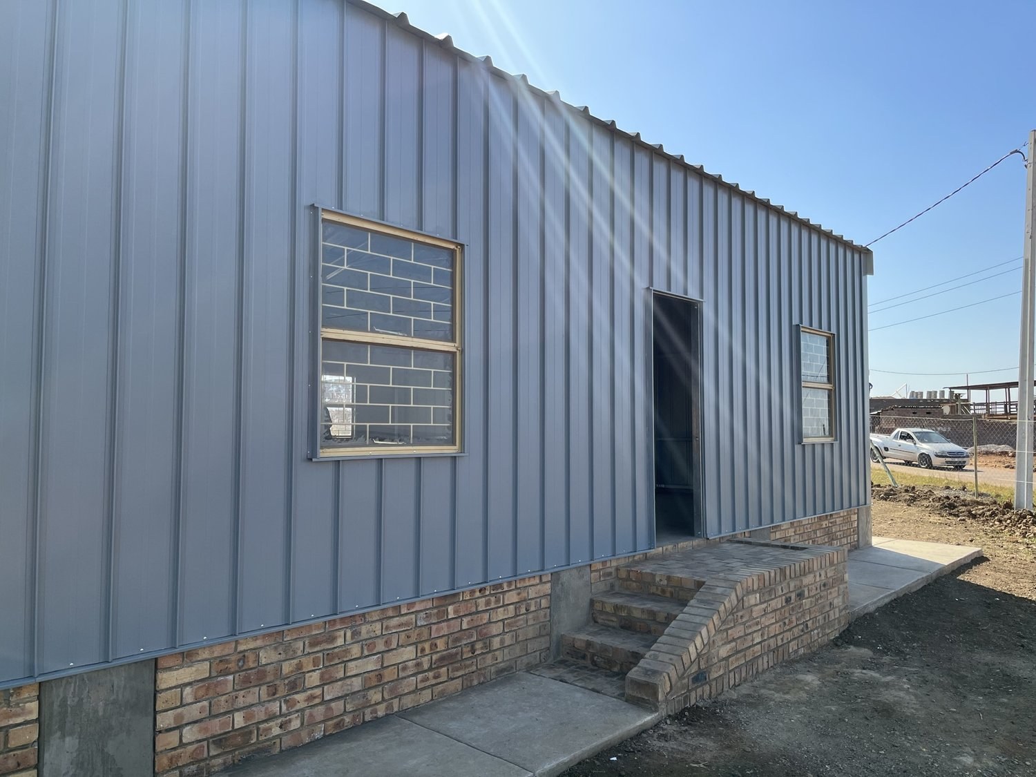 Side wall of a steel-clad building showing a window and open door above a brick base course