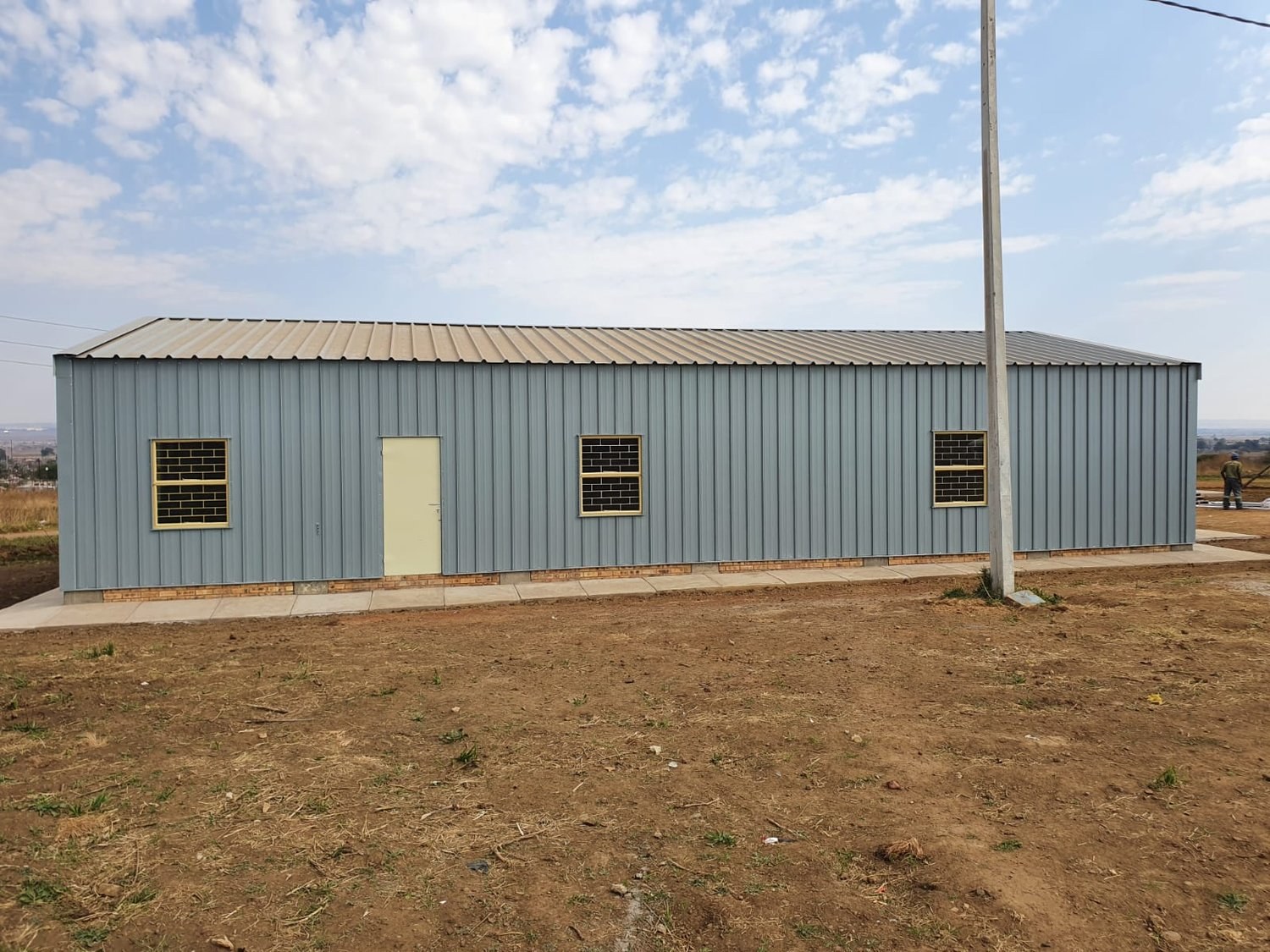 Finished steel-clad building with door and two windows set over a brick base course